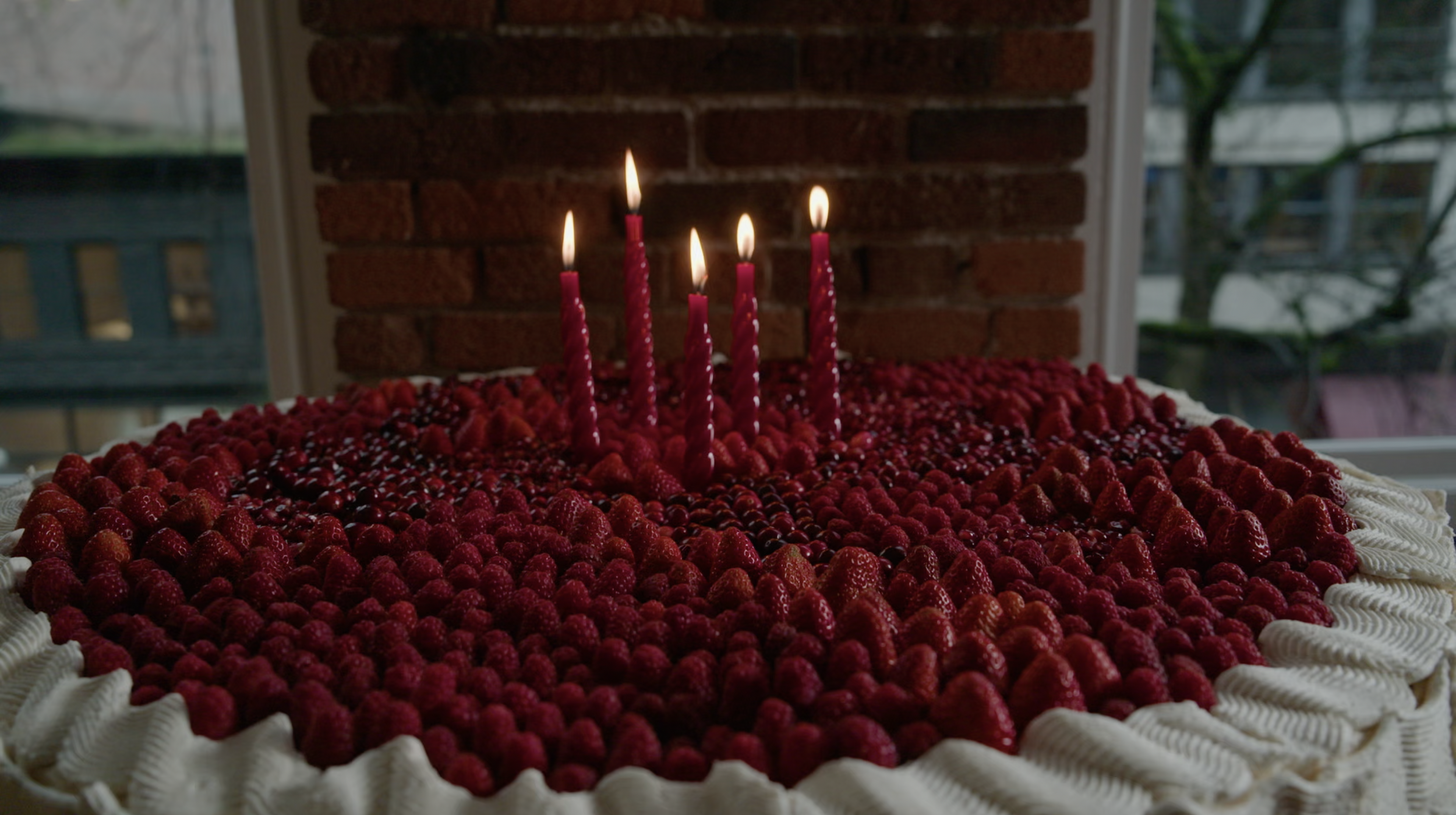 Large berry-topped cake with five lit red candles and whipped cream frosting
