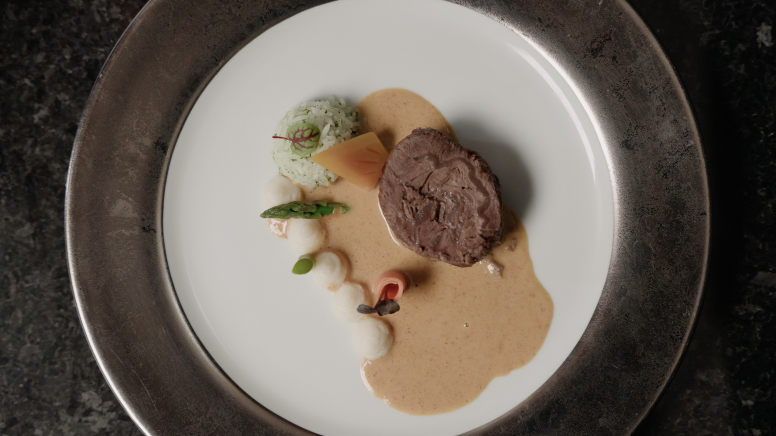 Gourmet beef tenderloin with rice, vegetables, and creamy sauce plated on a white dish