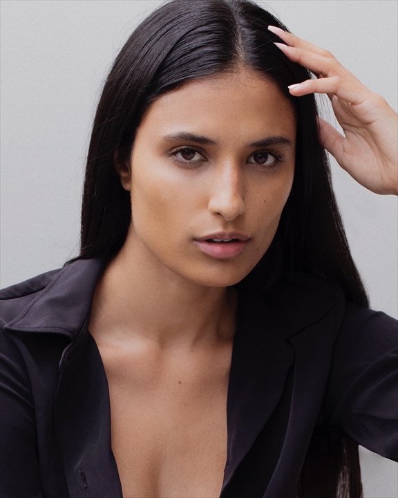 Close-up portrait of a woman with long dark hair wearing a black blazer against a gray background