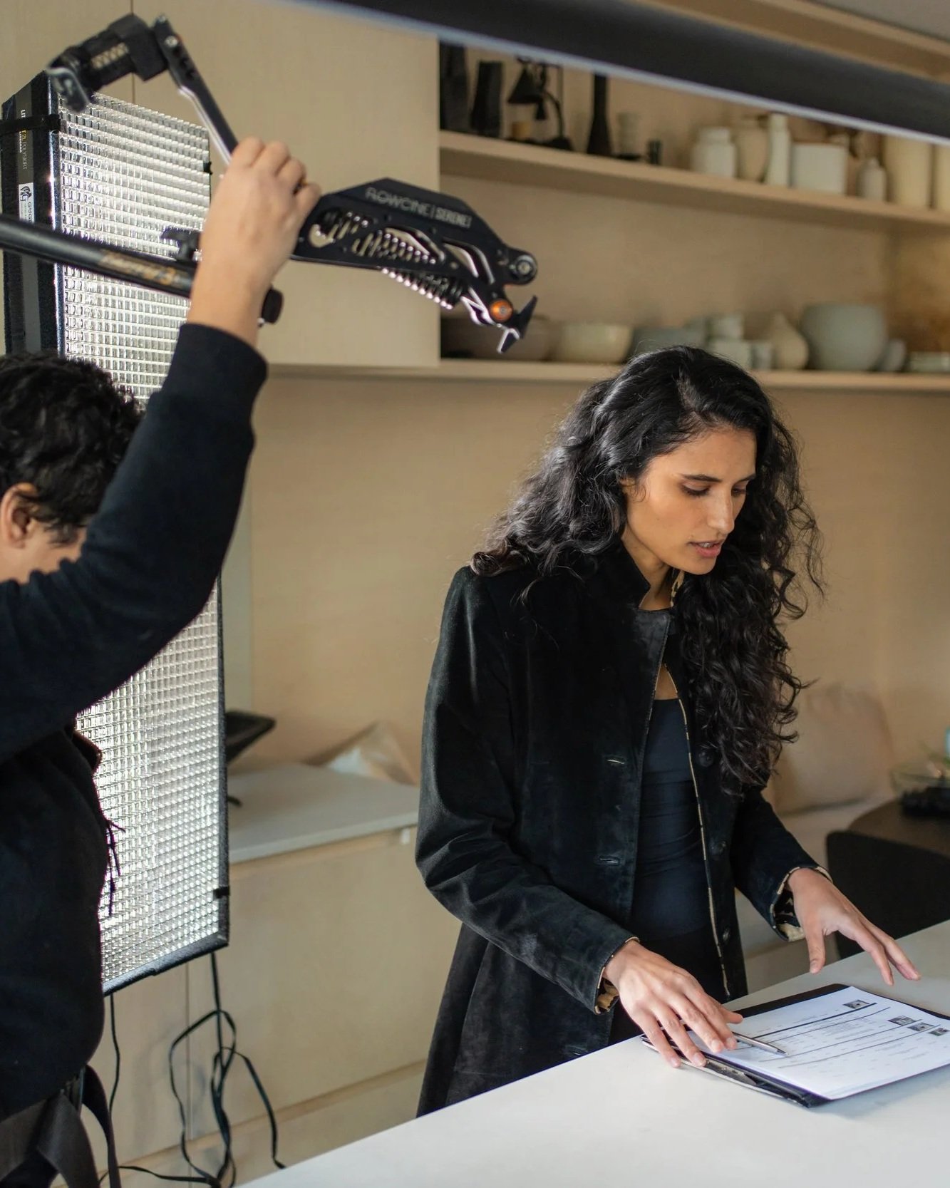 Woman reviewing a storyboard at a table while a crew member adjusts a studio light behind her