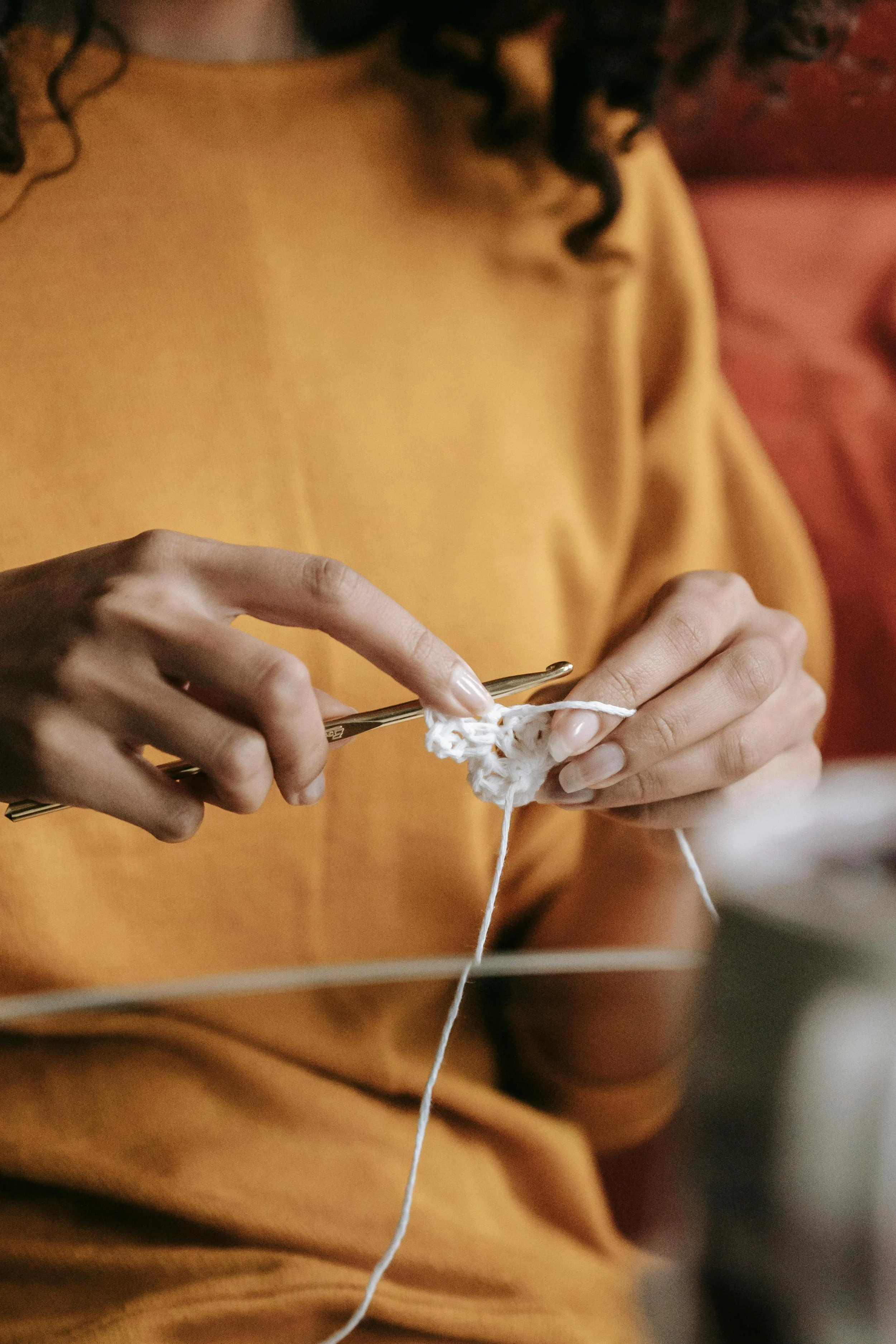 A person with curly dark hair knitting with white yarn using a metal crochet hook.