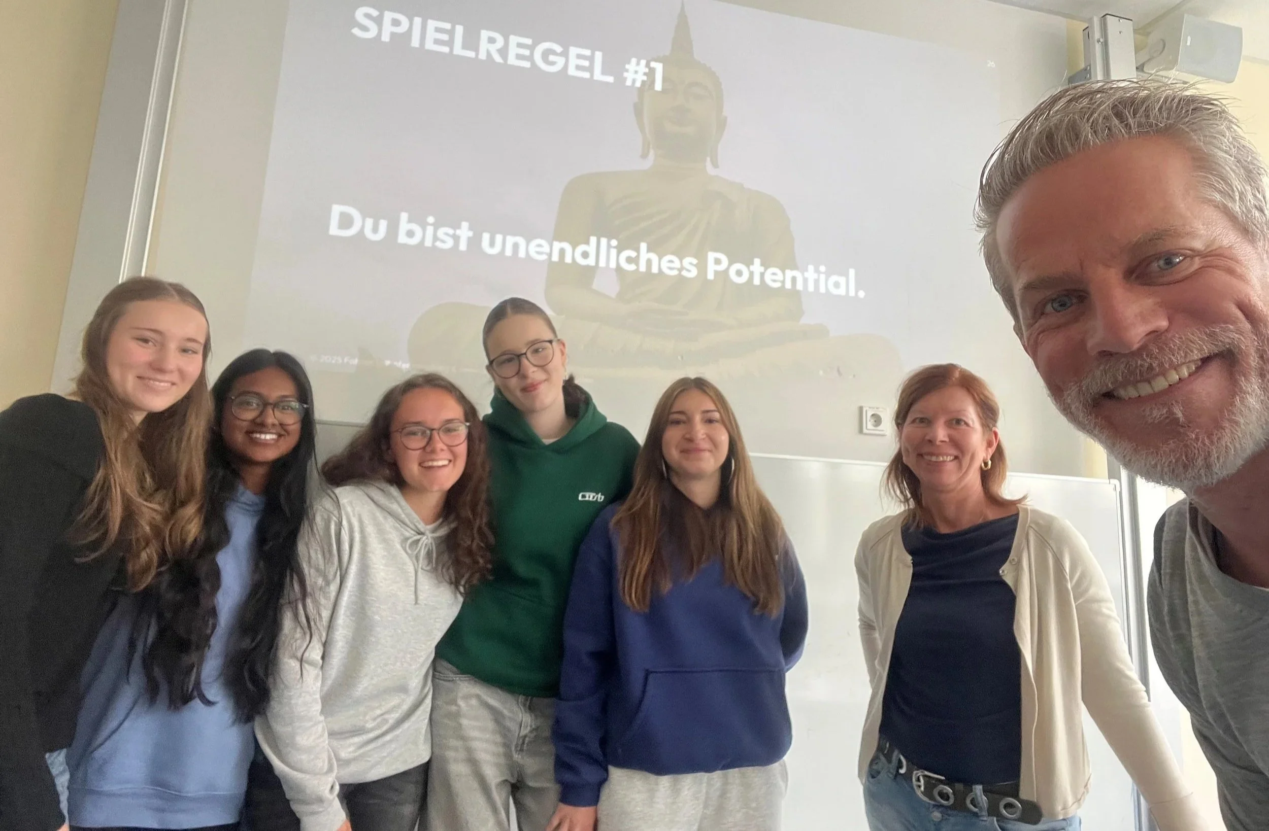 Gruppenfoto Workshop mit Fabian Erlhöfer und Barbara Kutschaty mit der Aufschrift 'SPIELREGEL #1' und 'Du bist unendliches Potenzial' in einem Raum.