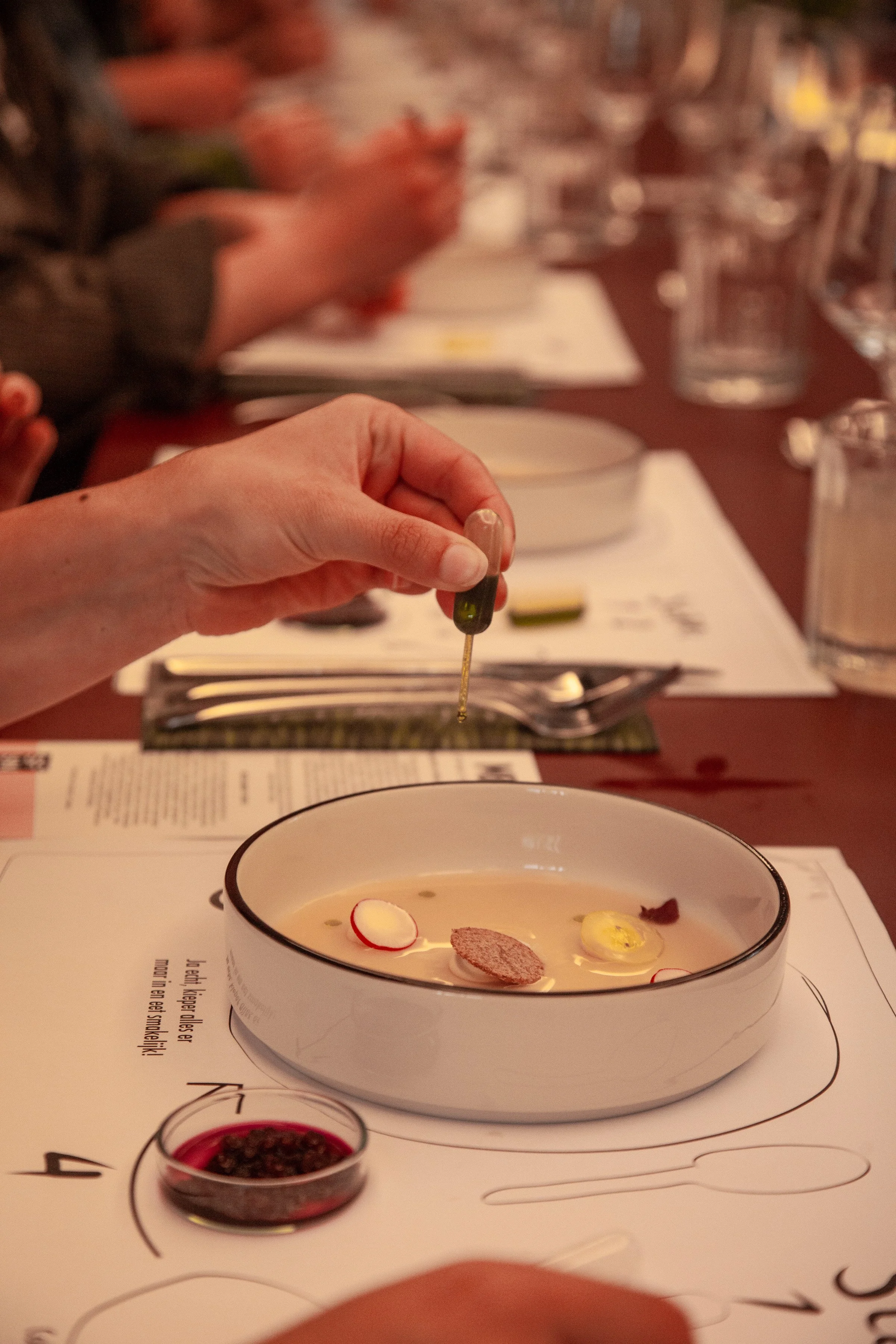 Bord met eten en een hand erboven met een pipet, waar olie uit druppelt