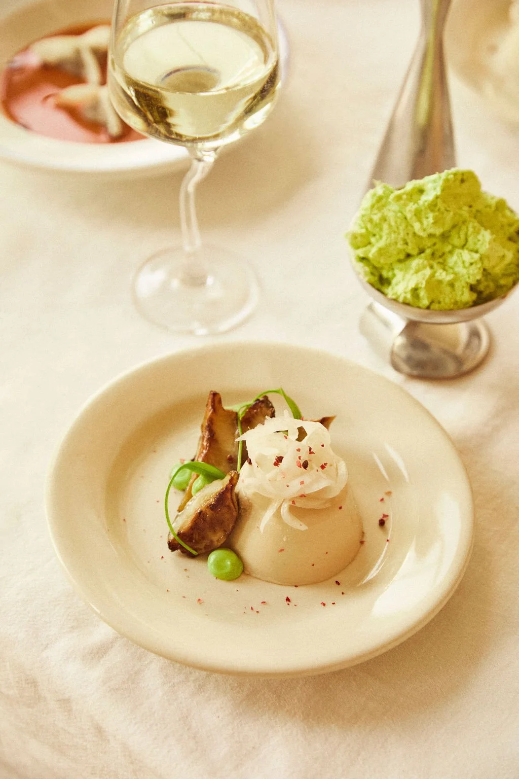 Gerecht met hazelnoot panna cotta met aardpeer, daslook mayonaise en ingelegde venkel, geserveerd met een glas witte wijn.
