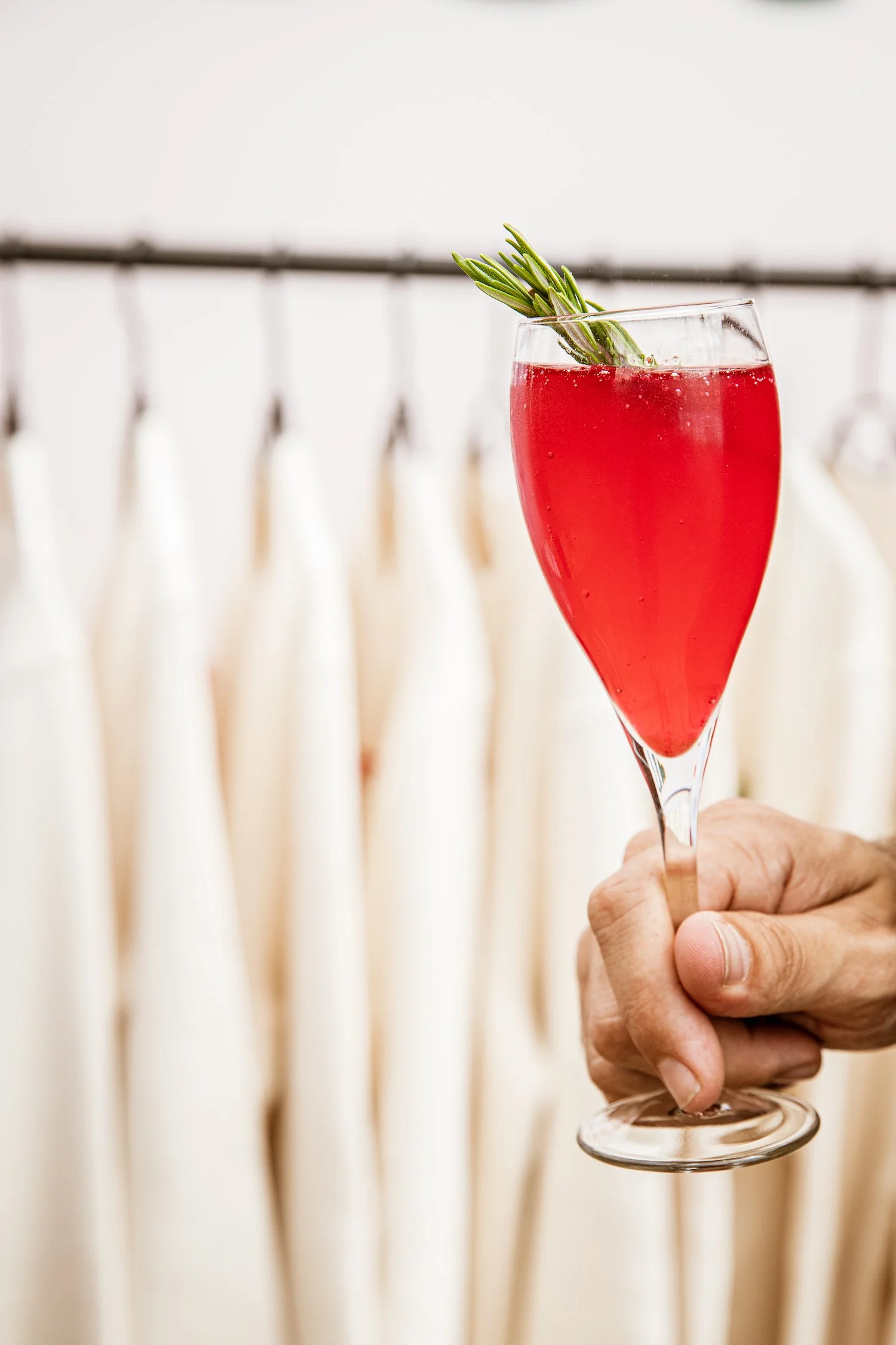 Hand die een glas met een bietenspritz vasthoudt, versierd met een takje rozemarijn.