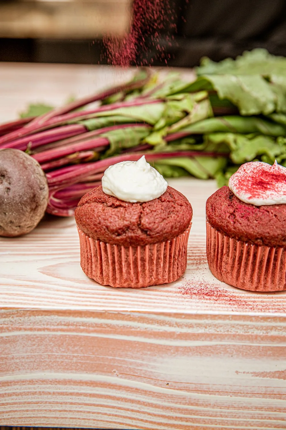 Twee bieten cupcakes met botercrème en bietenpoeder, op een houten tafel met bieten op de achtergrond.