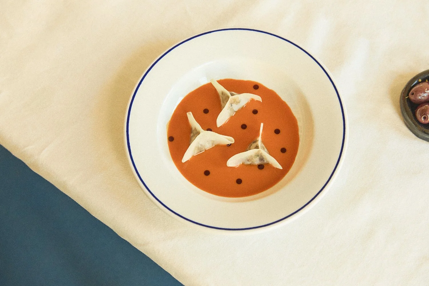 Een bord met een wortelsaus en vier dumplings met pompoenpitolie