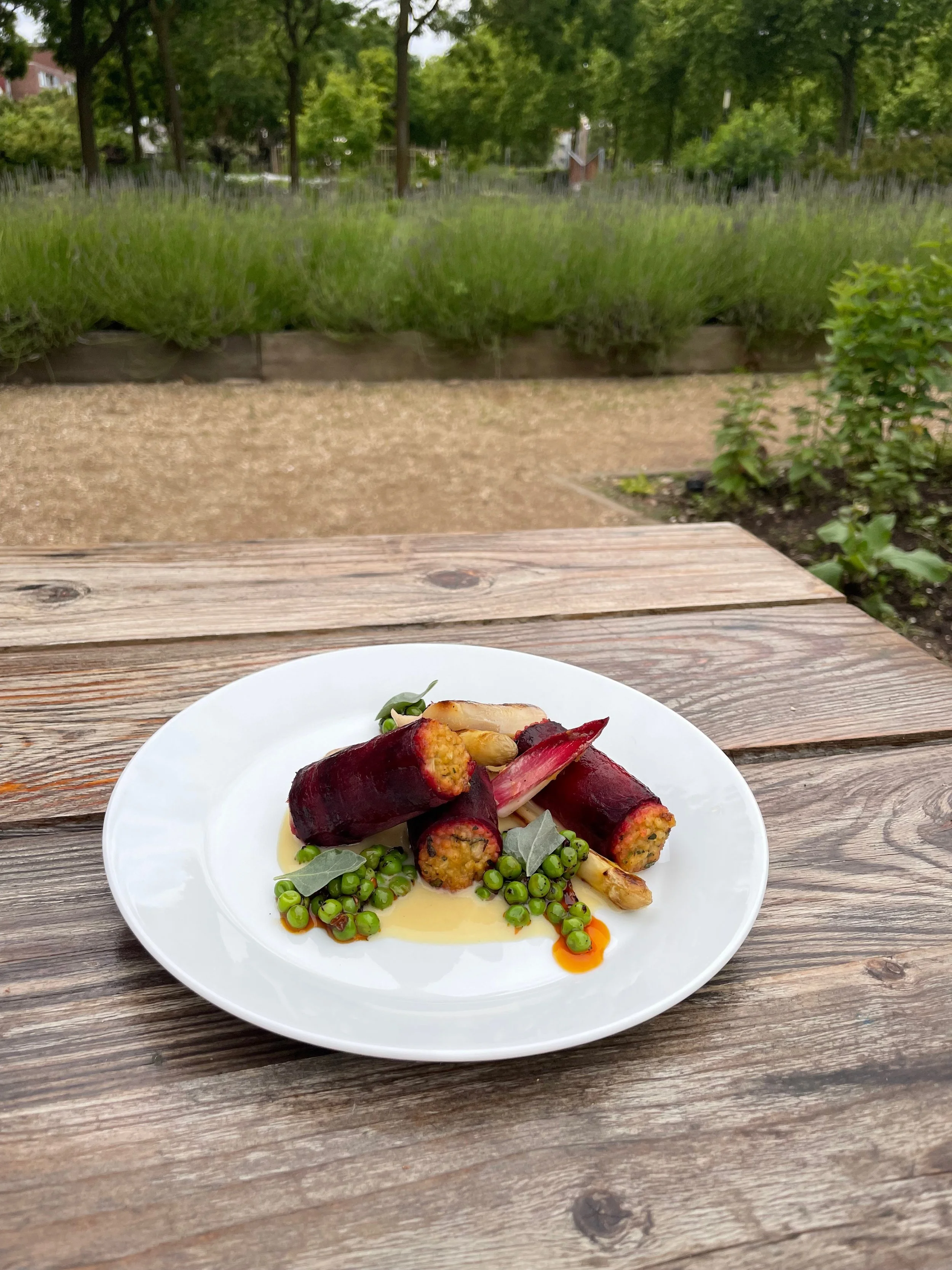 Een wit bord met gevuld gerecht op een houten tafel, met een achtergrond van een tuin met groen gras en bomen.