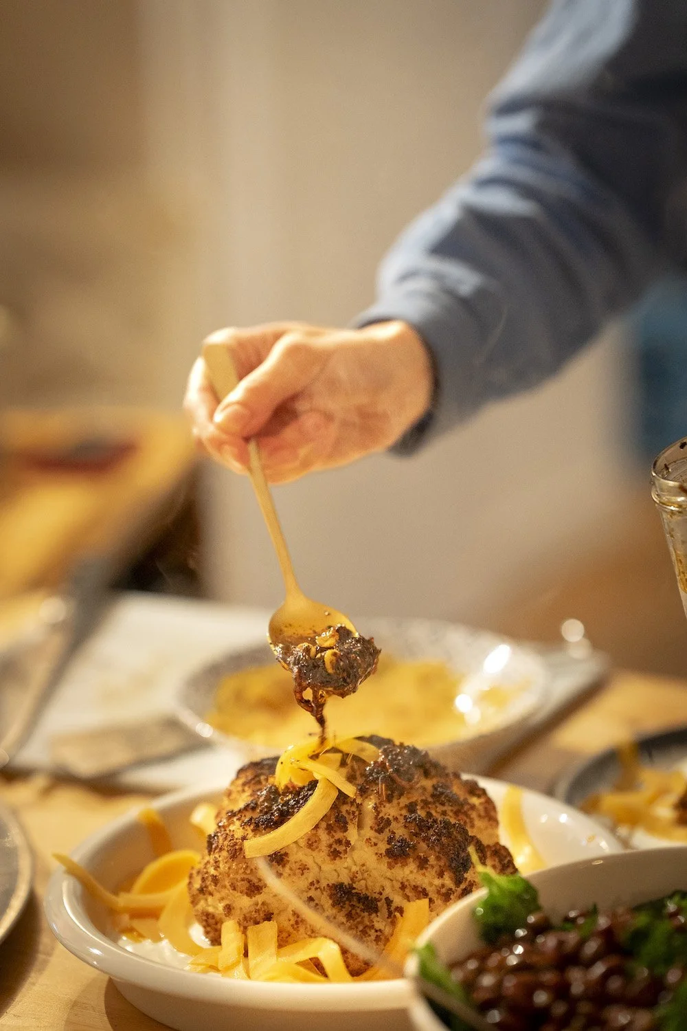 Persoon serveert een hele bloemkool met ingelegde pompoen en chili olie op een bord.