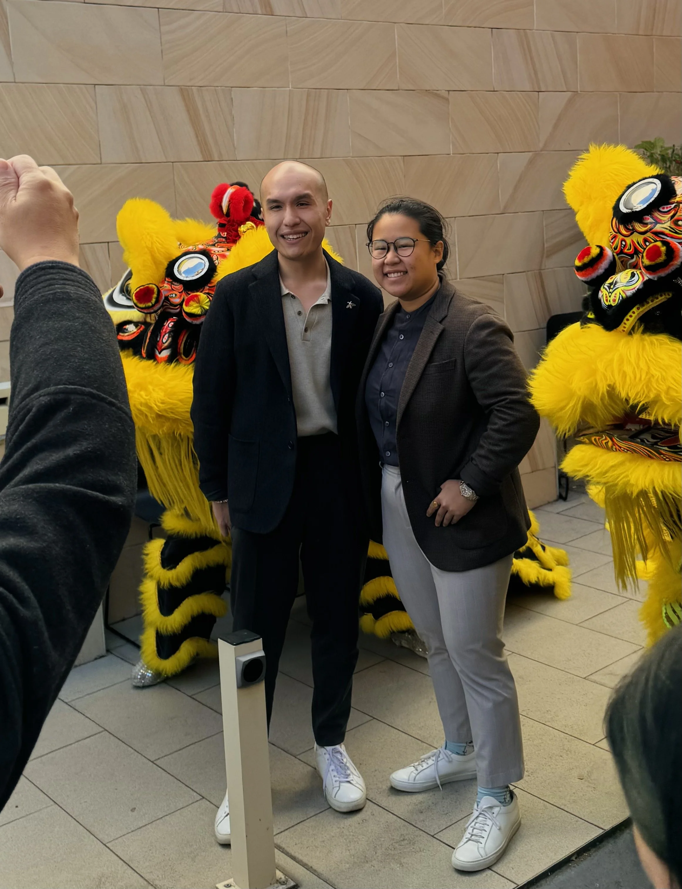 Two people standing in front of Chinese lion dance costumes, taking a photo together.