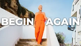 A woman in an orange outfit standing outdoors on stairs, with the words 'BEGIN AGAIN' overlaid.