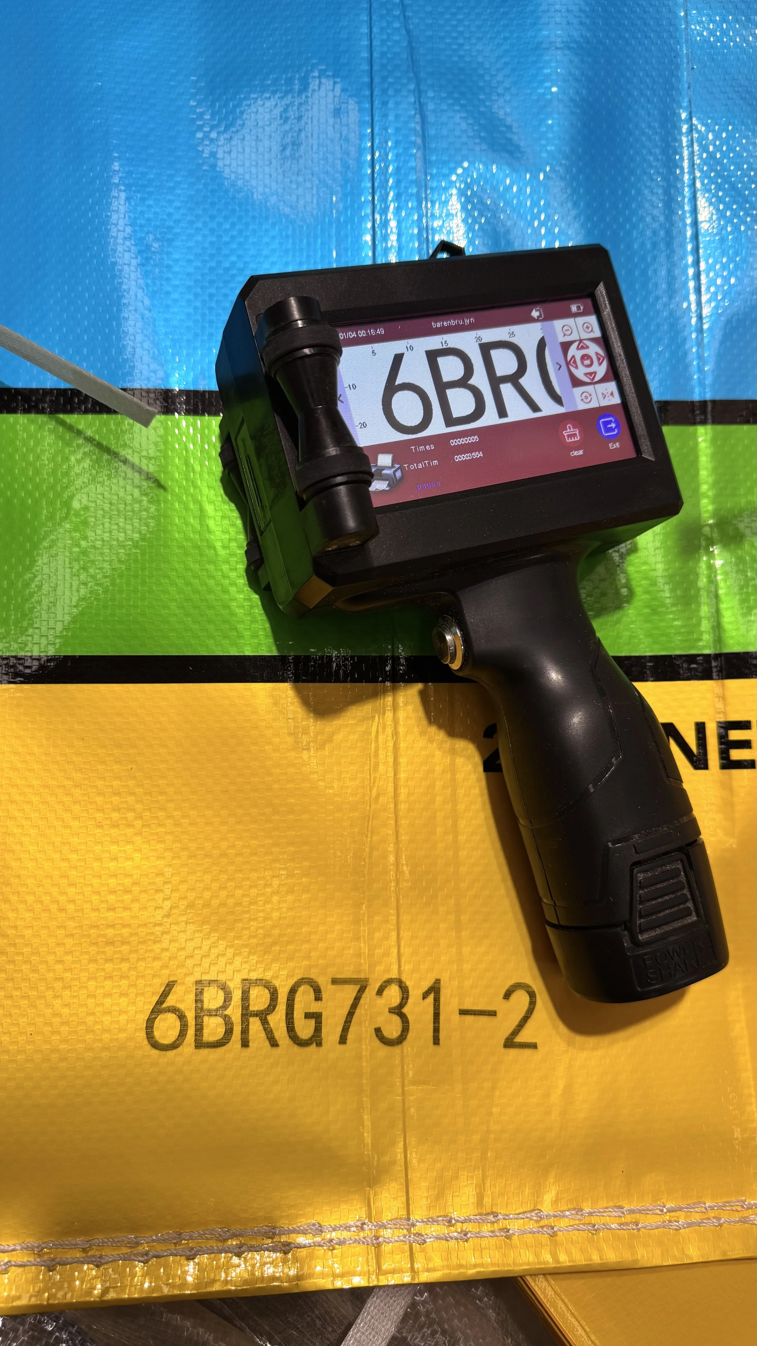 A handheld barcode scanner displaying '6BRG' on its screen, resting on a colorful safety line with yellow, green, and blue sections.