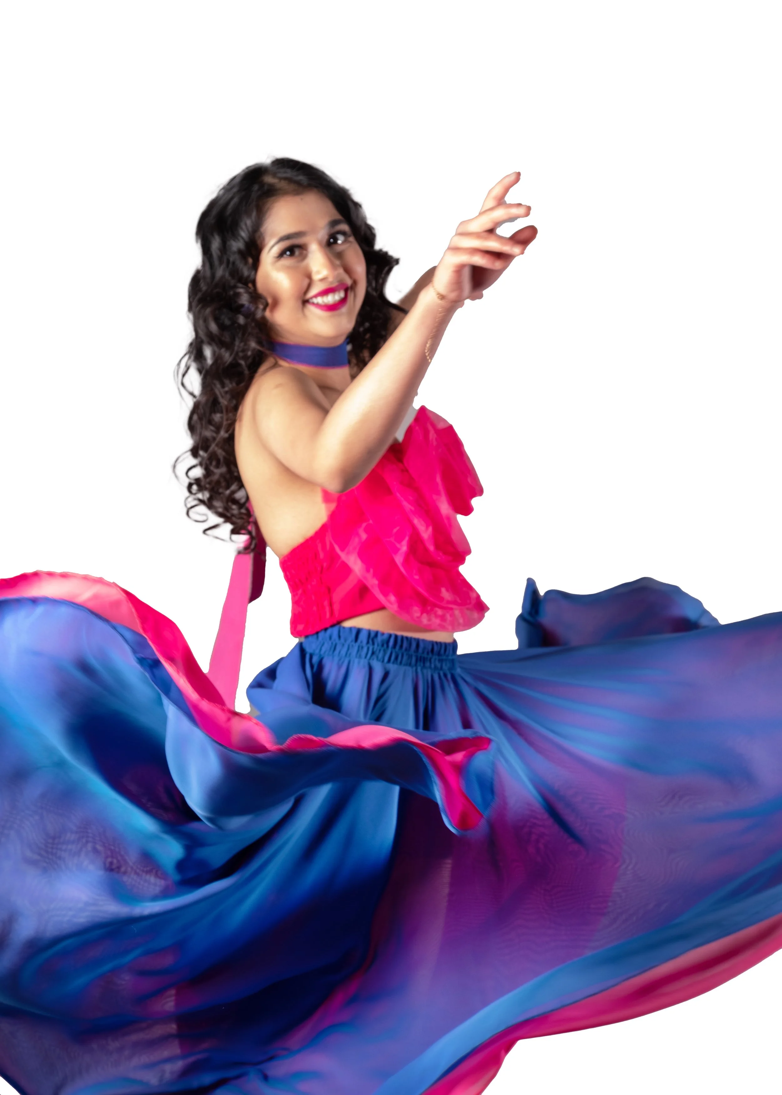 A woman with curly dark hair, wearing bright makeup, a pink strapless top, and blue skirt, smiling and gesturing with her hand against a white background.