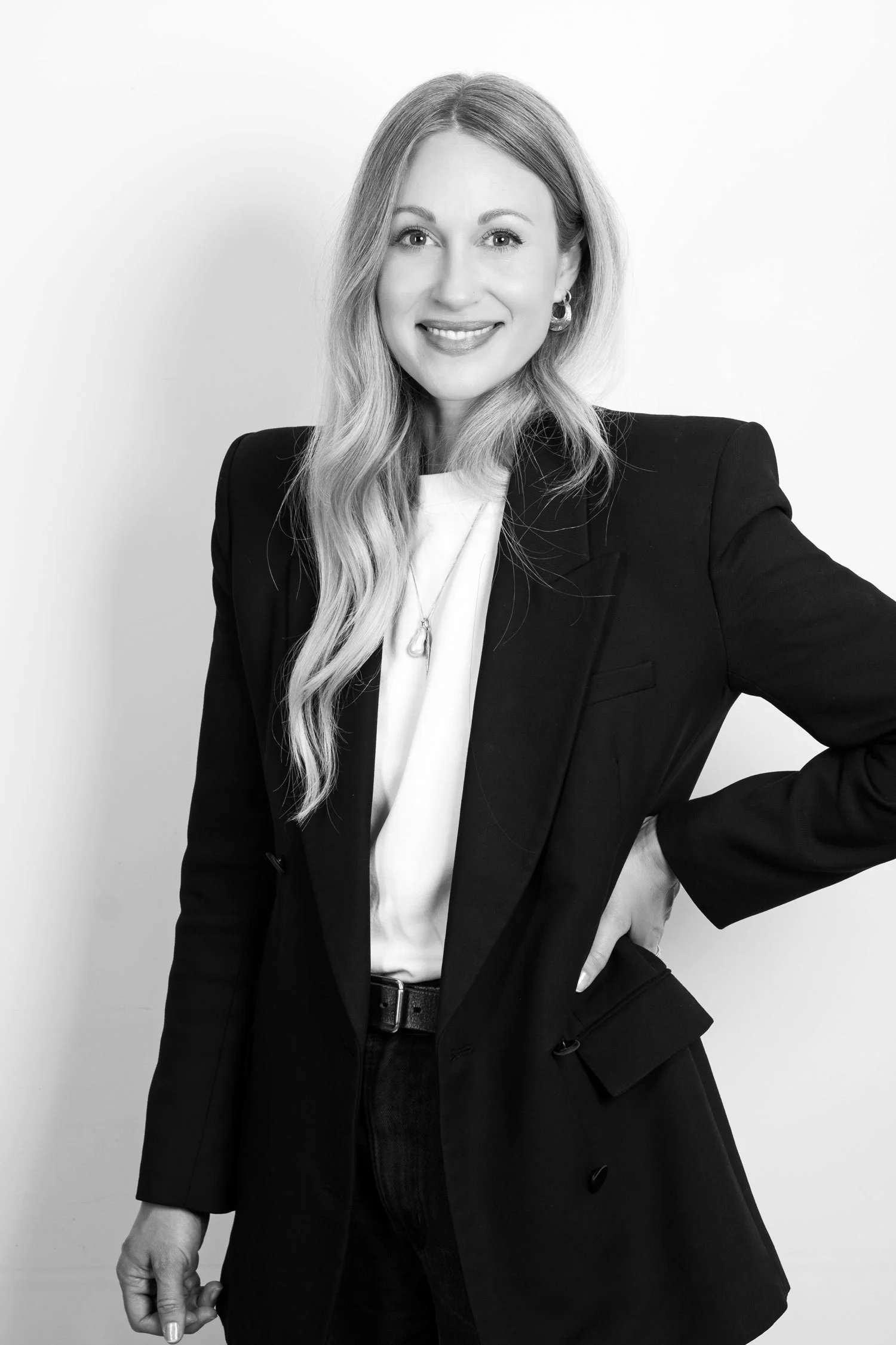 Black and white portrait of a woman smiling, dressed in a black blazer and white blouse, standing against a plain backdrop.