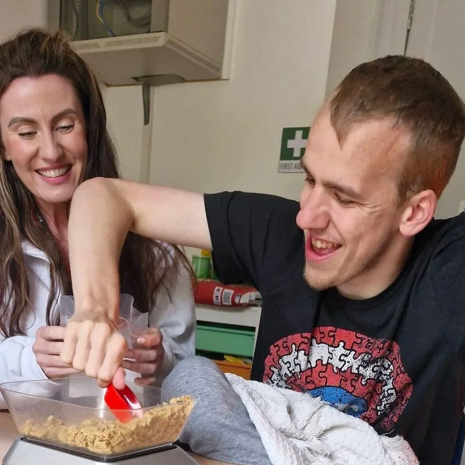 A man with a prosthetic arm eating cereal with a woman smiling beside him.