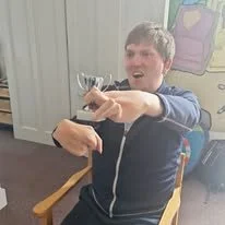 Young boy sitting in a chair, holding a small trophy, smiling, indoors.