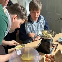 Two young boys cooking eggs on a stovetop in a kitchen.