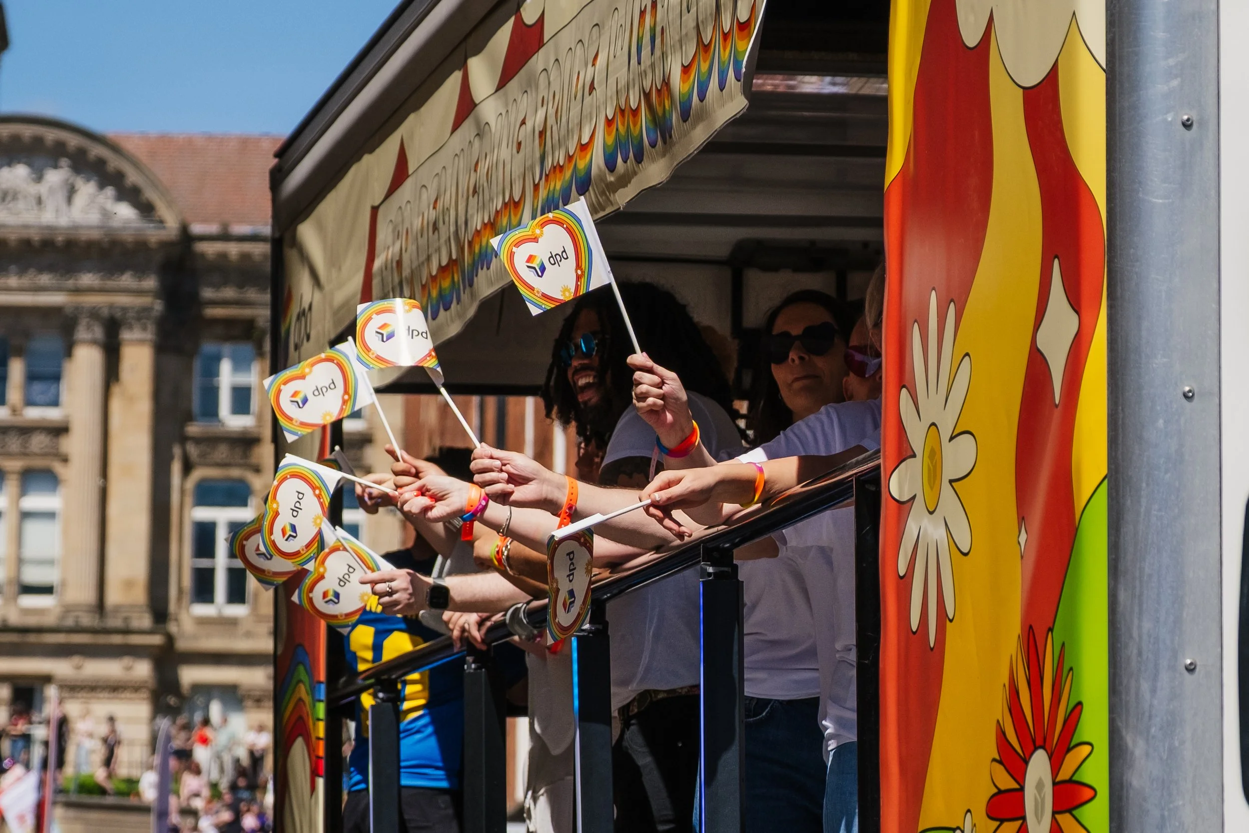 People riding a carnival or parade float decorated with rainbow flags and vibrant designs, waving to the crowd.