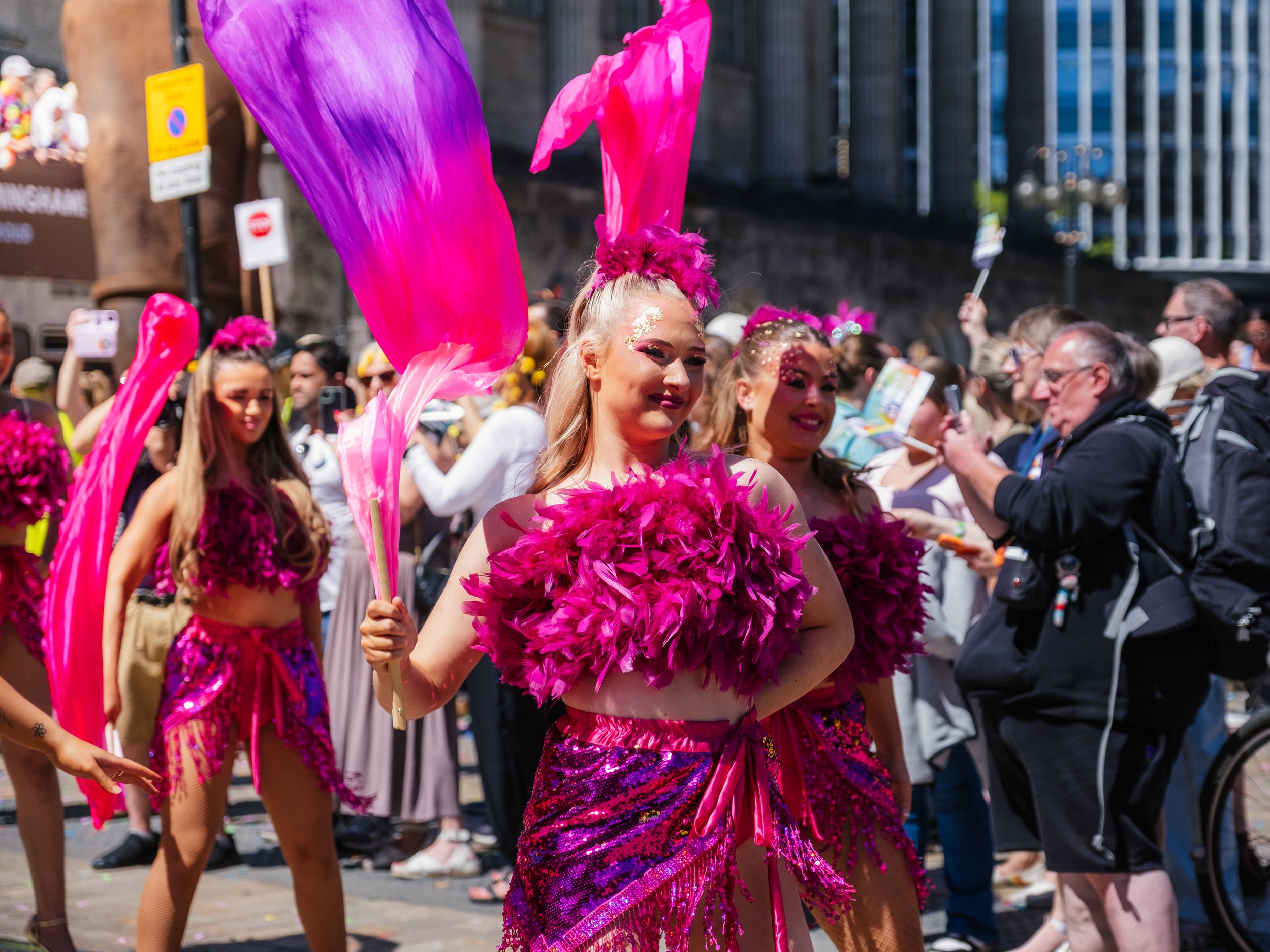 A group of women dressed in vibrant pink costumes with feathers and sequins participating in a parade.