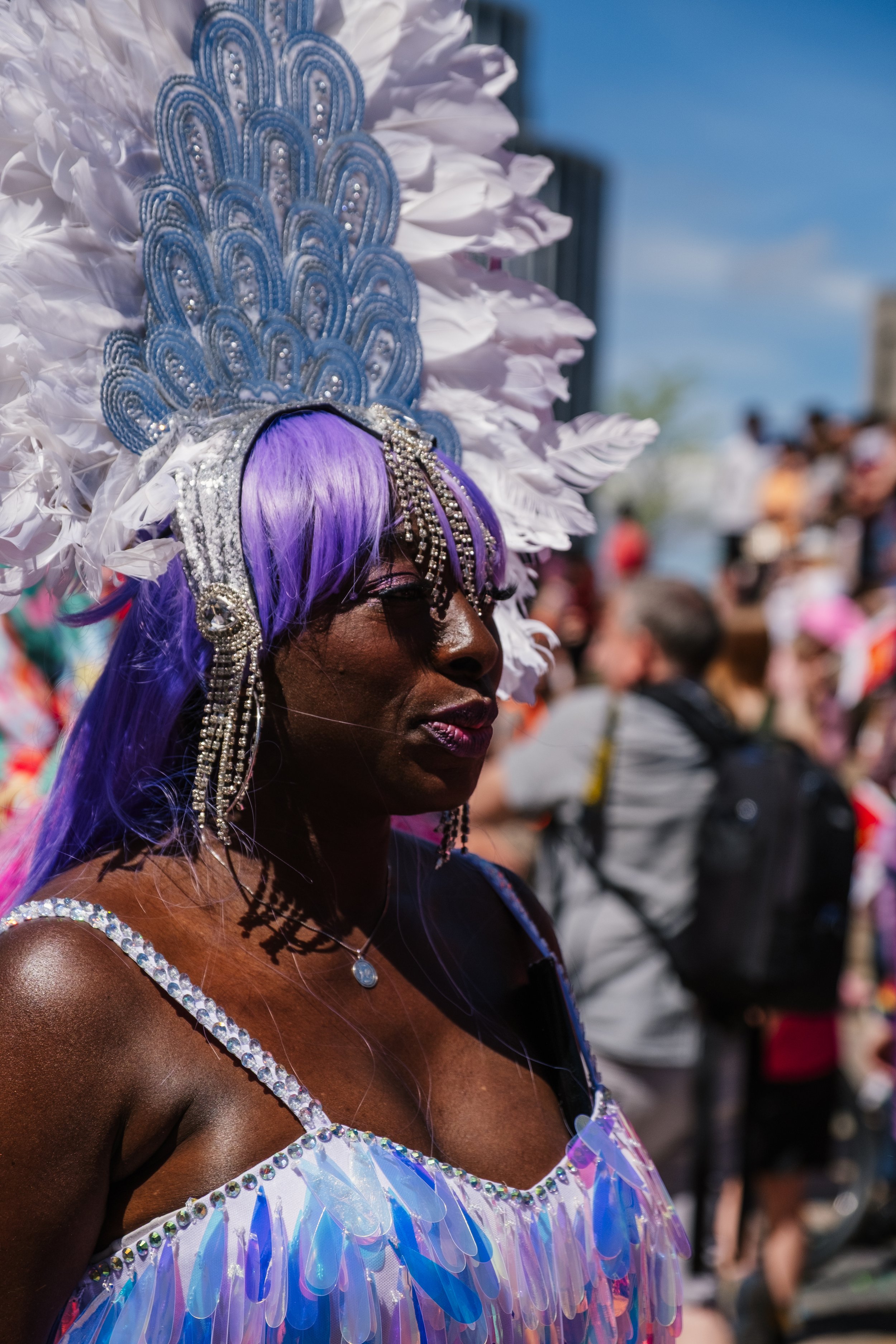 Person wearing a colorful sequined costume and an elaborate feathered headdress at a parade.