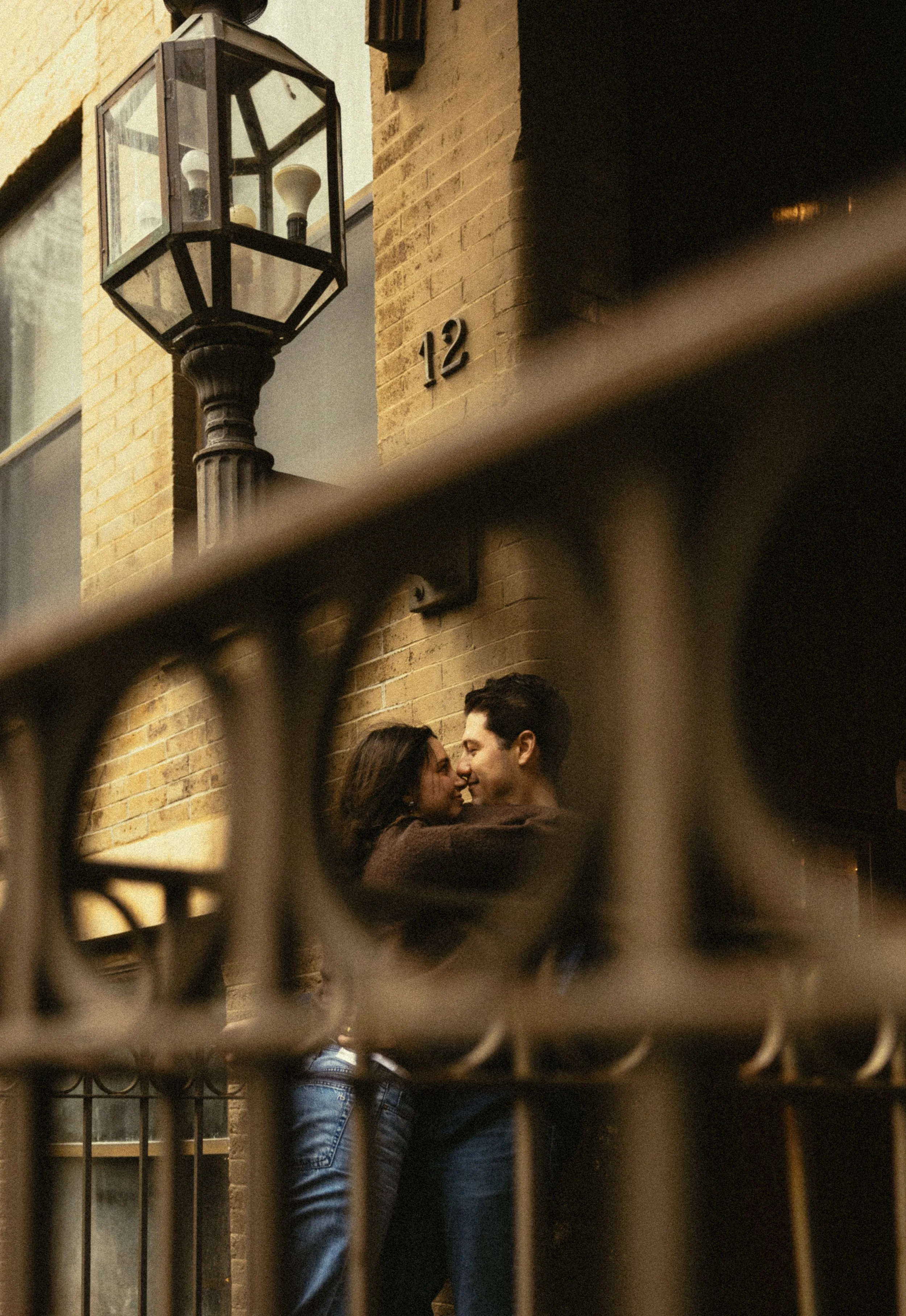 A couple kissing through a fence on a city street at night.