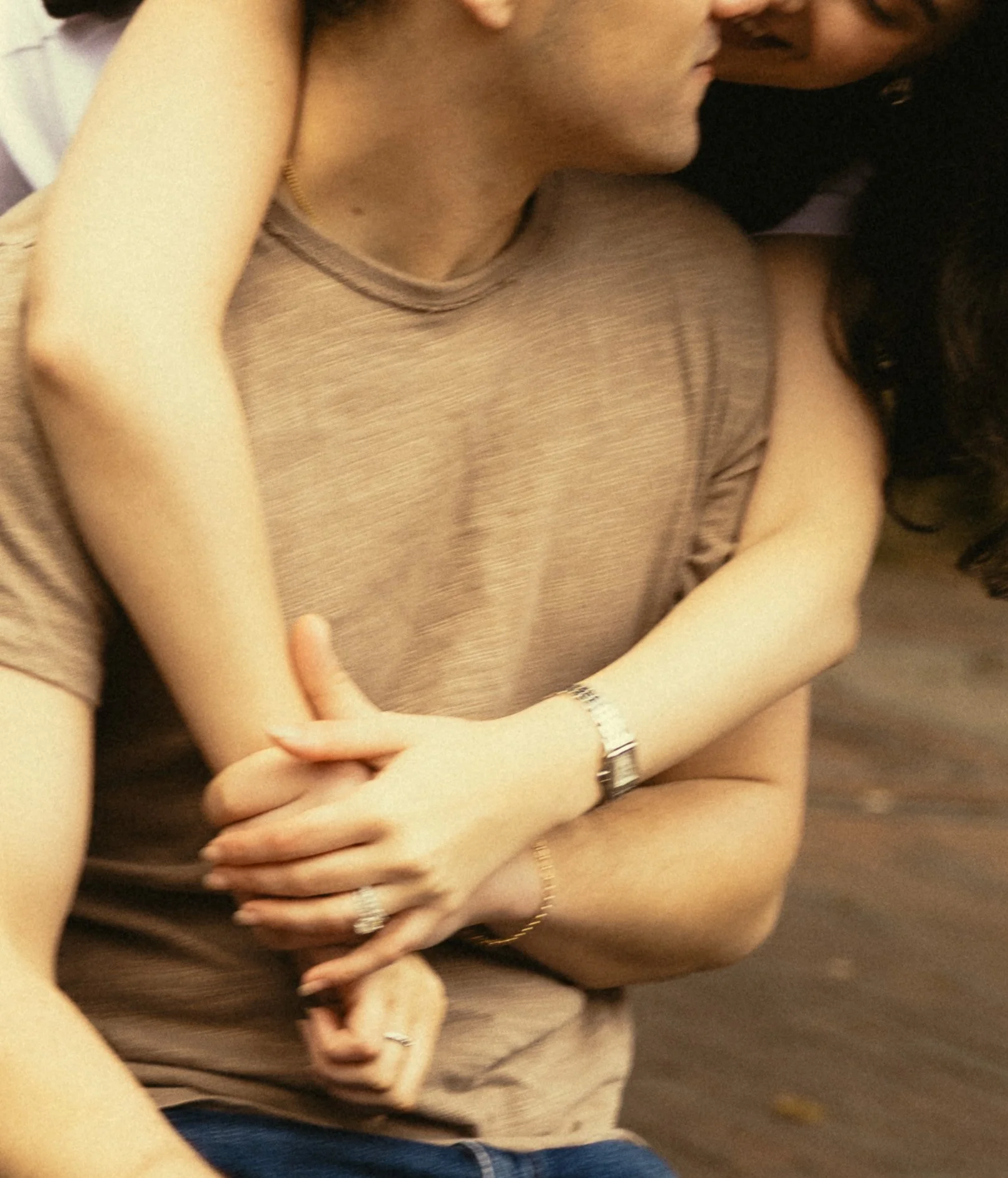 Close-up of a person with their arms crossed and their face partially visible, wearing a beige sleeveless top and a watch on their wrist.