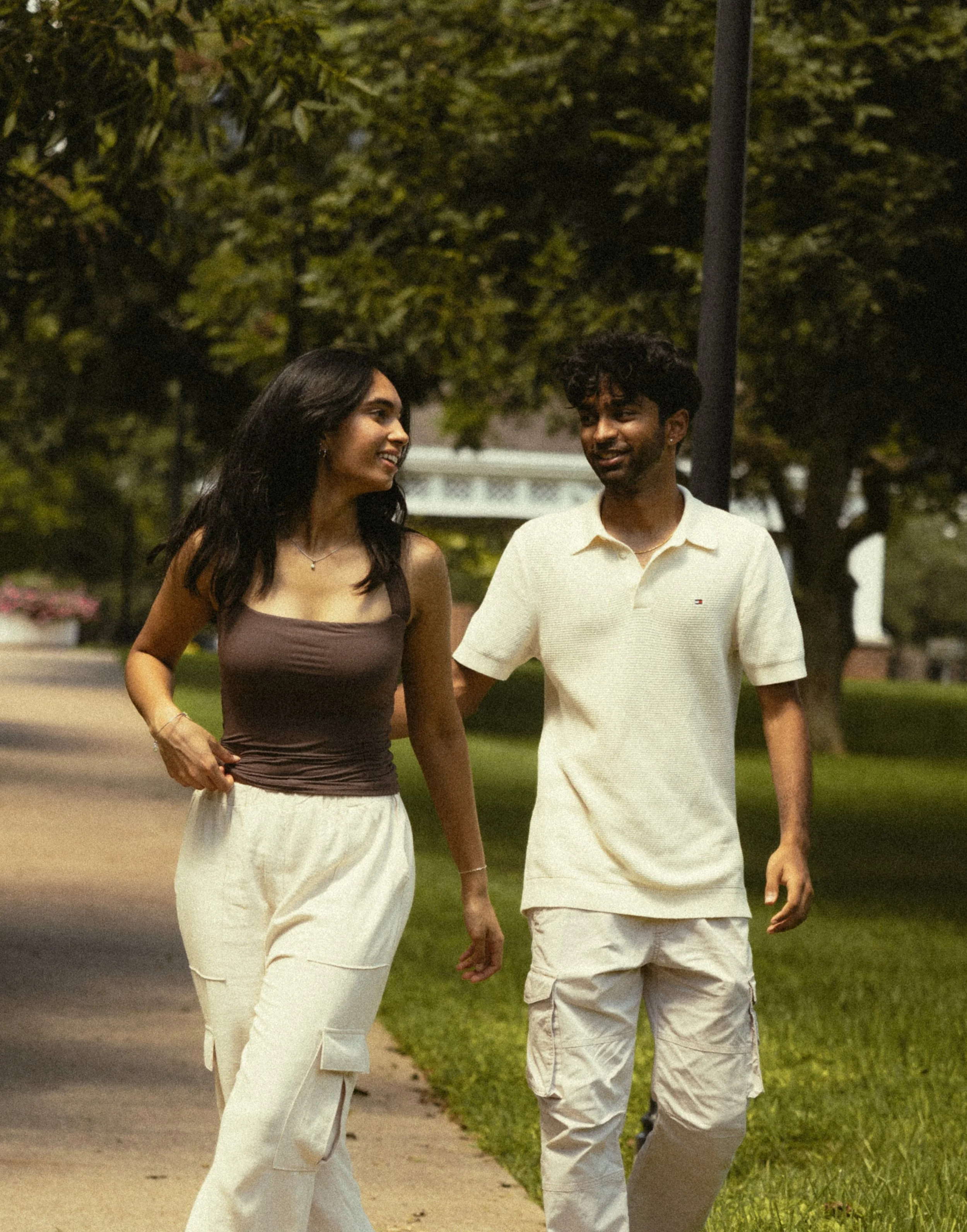 A young couple walking together outdoors at night, smiling and engaging in conversation, with trees in the background.