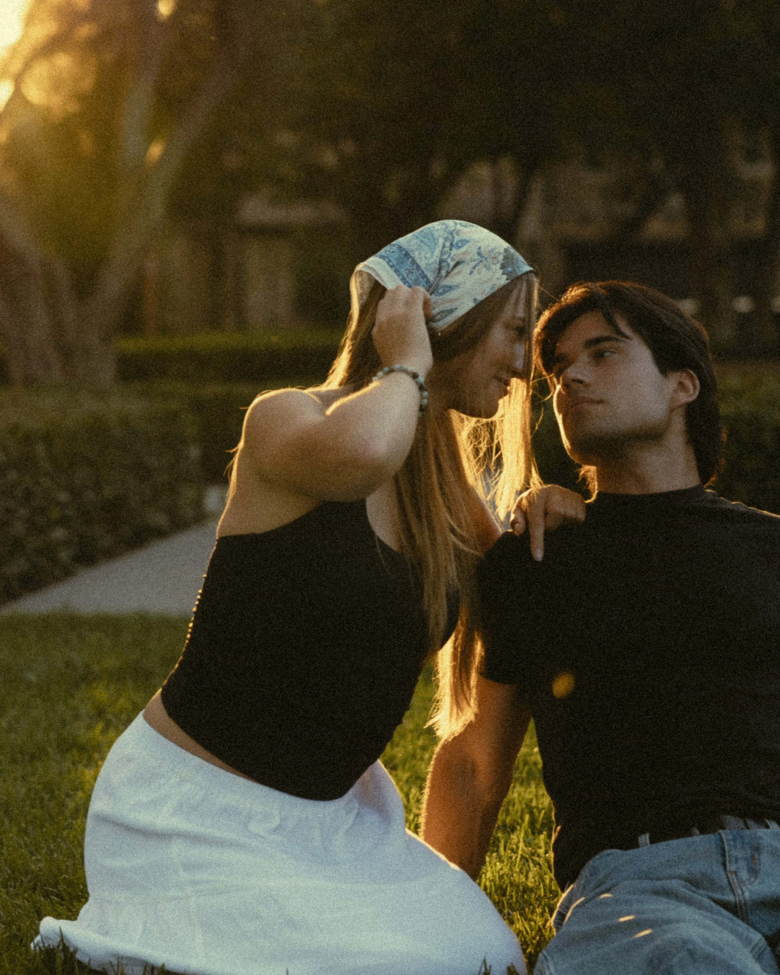 A young couple sitting on grass during sunset, facing each other and smiling, holding hands gently