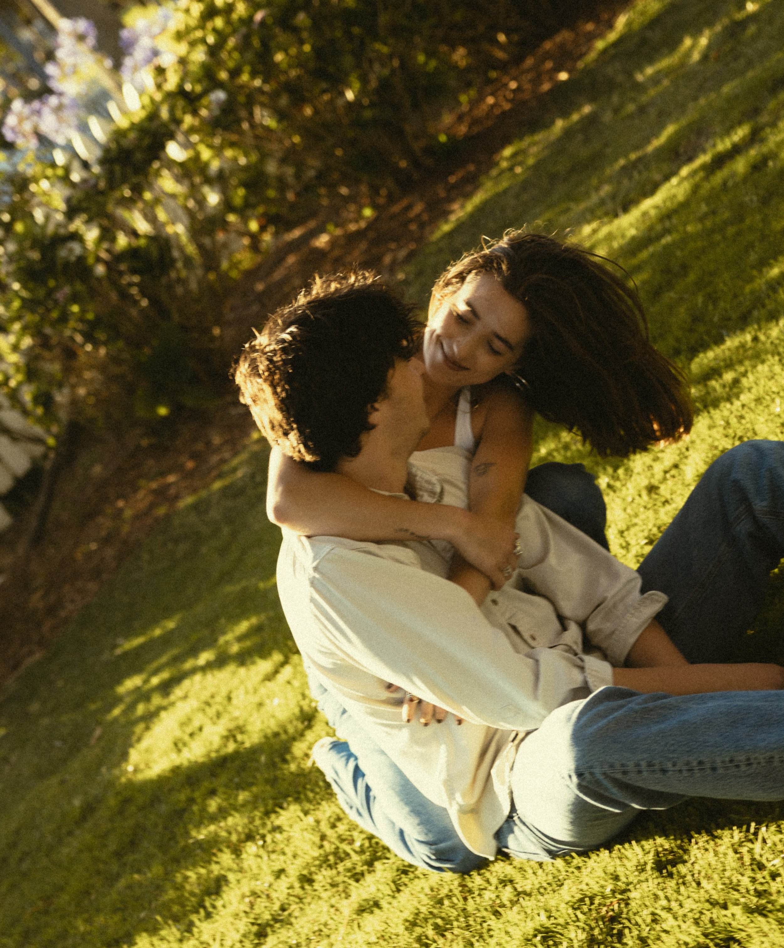 A woman smiling and embracing a person outside in a park during the daytime, with lush green trees in the background.