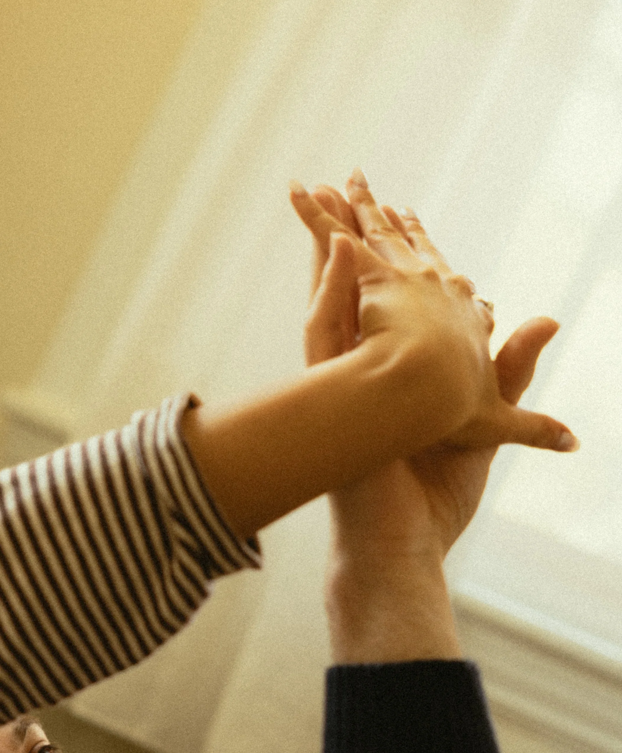 Close-up of a person's hand and fingers, with a blurred background and part of a striped sleeve visible.