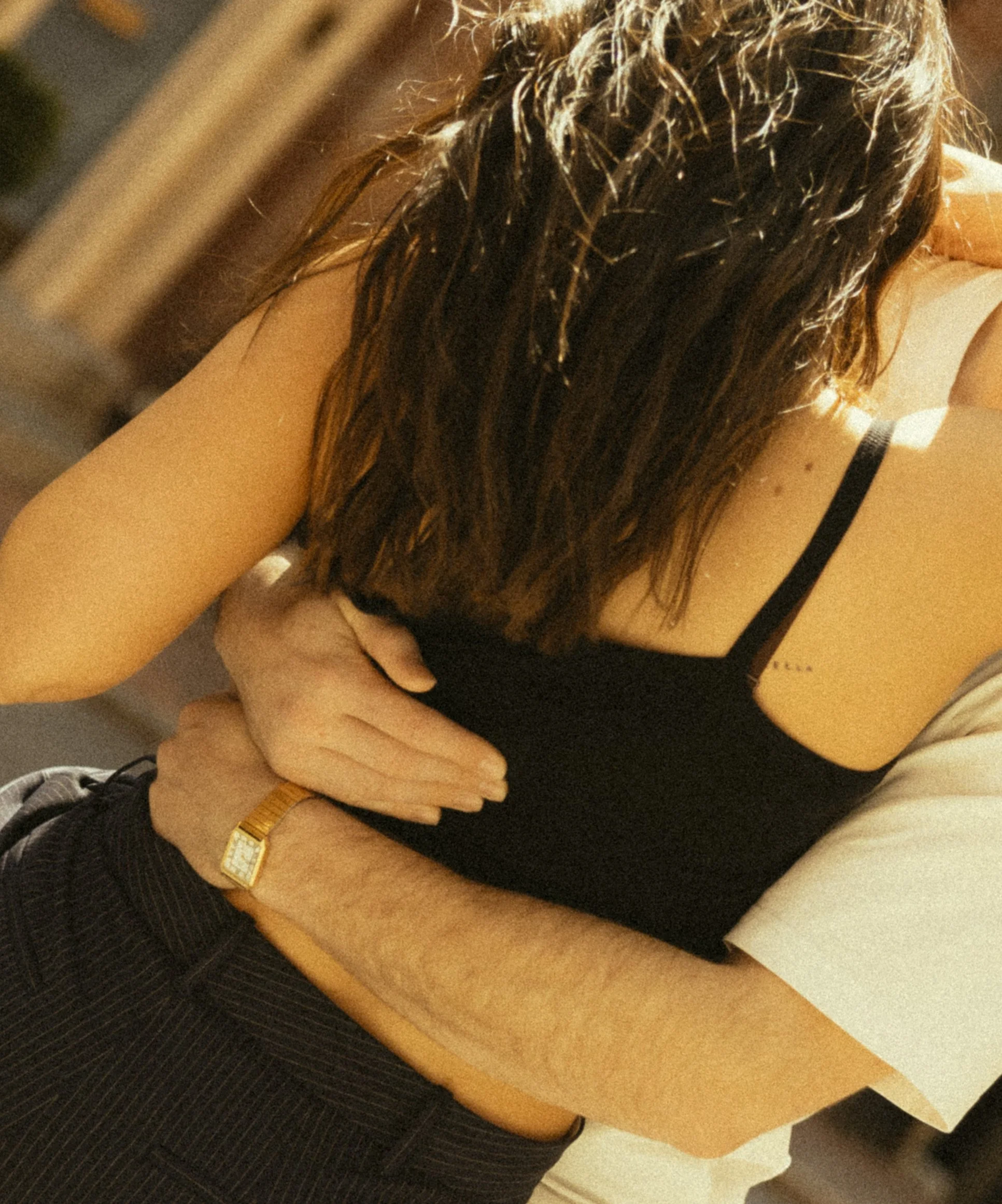 A woman with wet or greasy hair is resting her arms on a table, with her head leaning forward. She is wearing a black sleeveless top and a gold wristwatch.