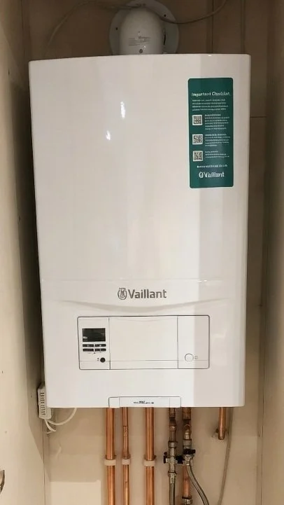 A white Vaillant tankless water heater mounted on a wall with copper pipes connected at the bottom.