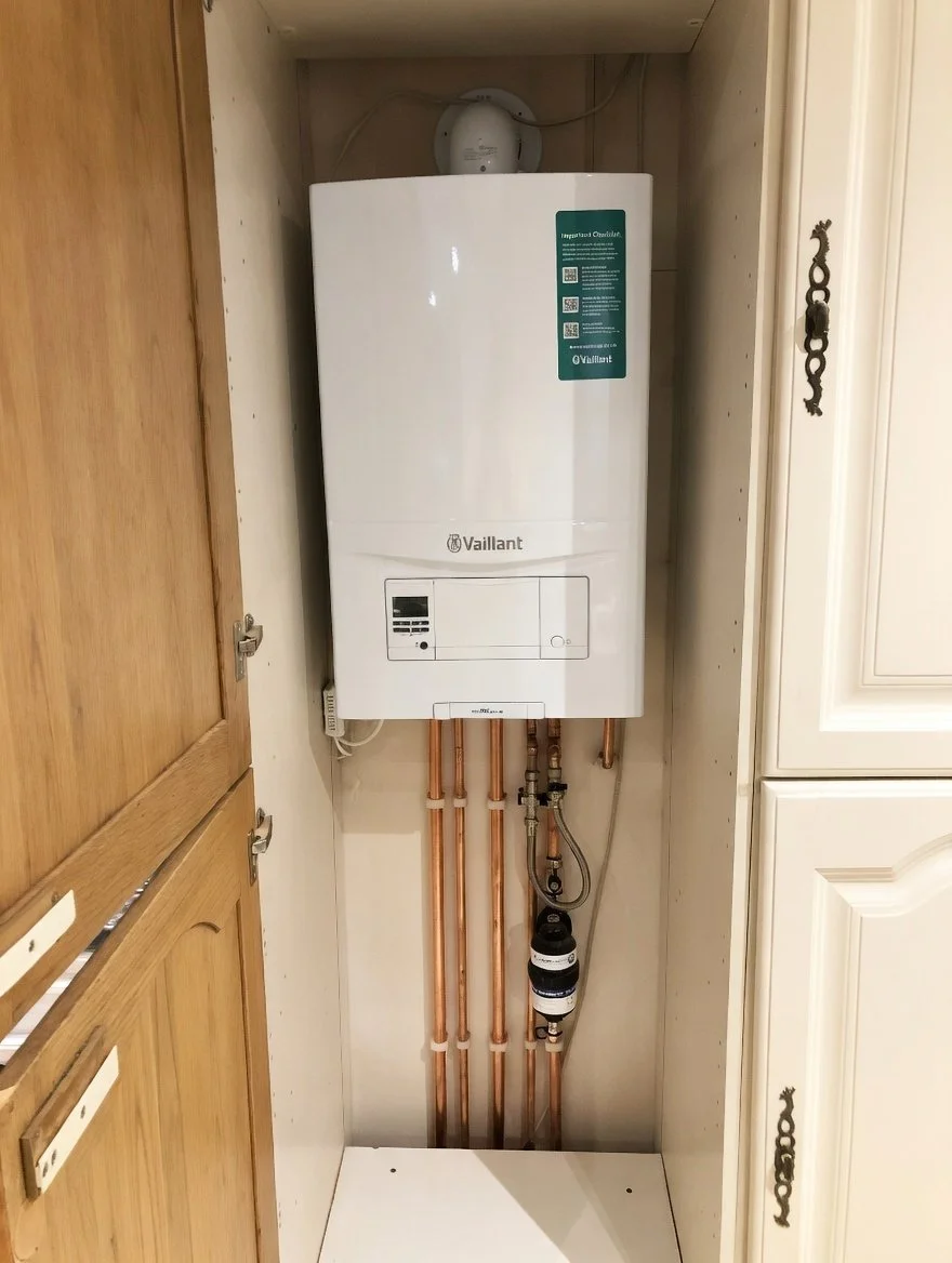 A white Vaillant tankless water heater installed in a small cabinet with copper pipes running down from it.