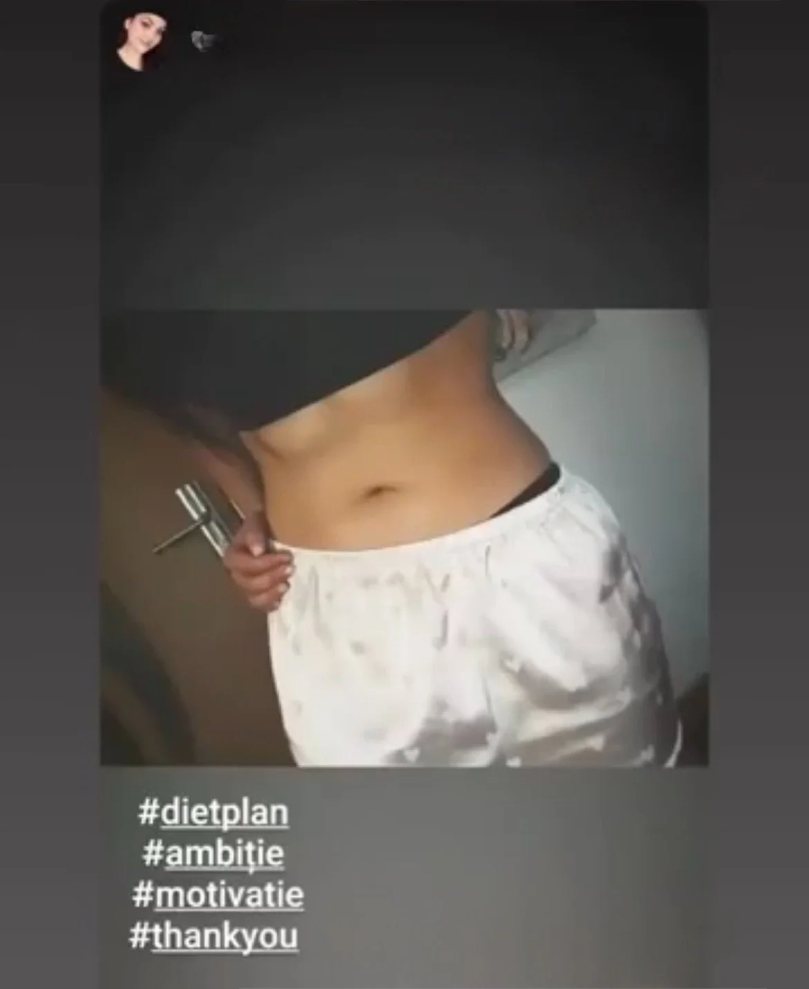Close-up of a person waist and stomach, wearing white shorts, holding a dumbbell, with hashtags #dietplan, #ambitie, #motivatie, #thankyou listed at the bottom.
