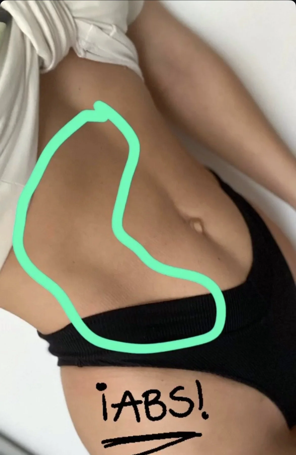 Close-up of a person's midsection wearing black underwear with a handwritten note that says '¡ABS!' and a green outline of abdominal muscles drawn over the stomach area.