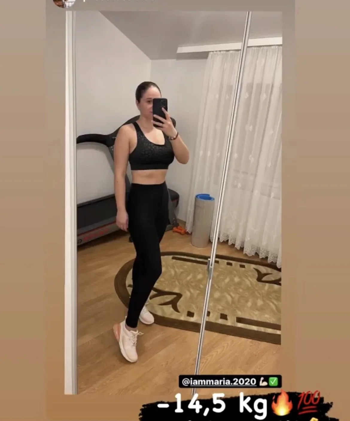A woman taking a mirror selfie in a room with a treadmill, a carpet, and curtains, showing her fitness progress of losing 14.5 kilograms.