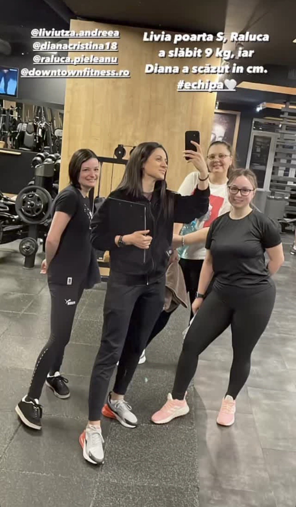 Group of four women taking a mirror selfie in a gym, with workout equipment visible in the background.