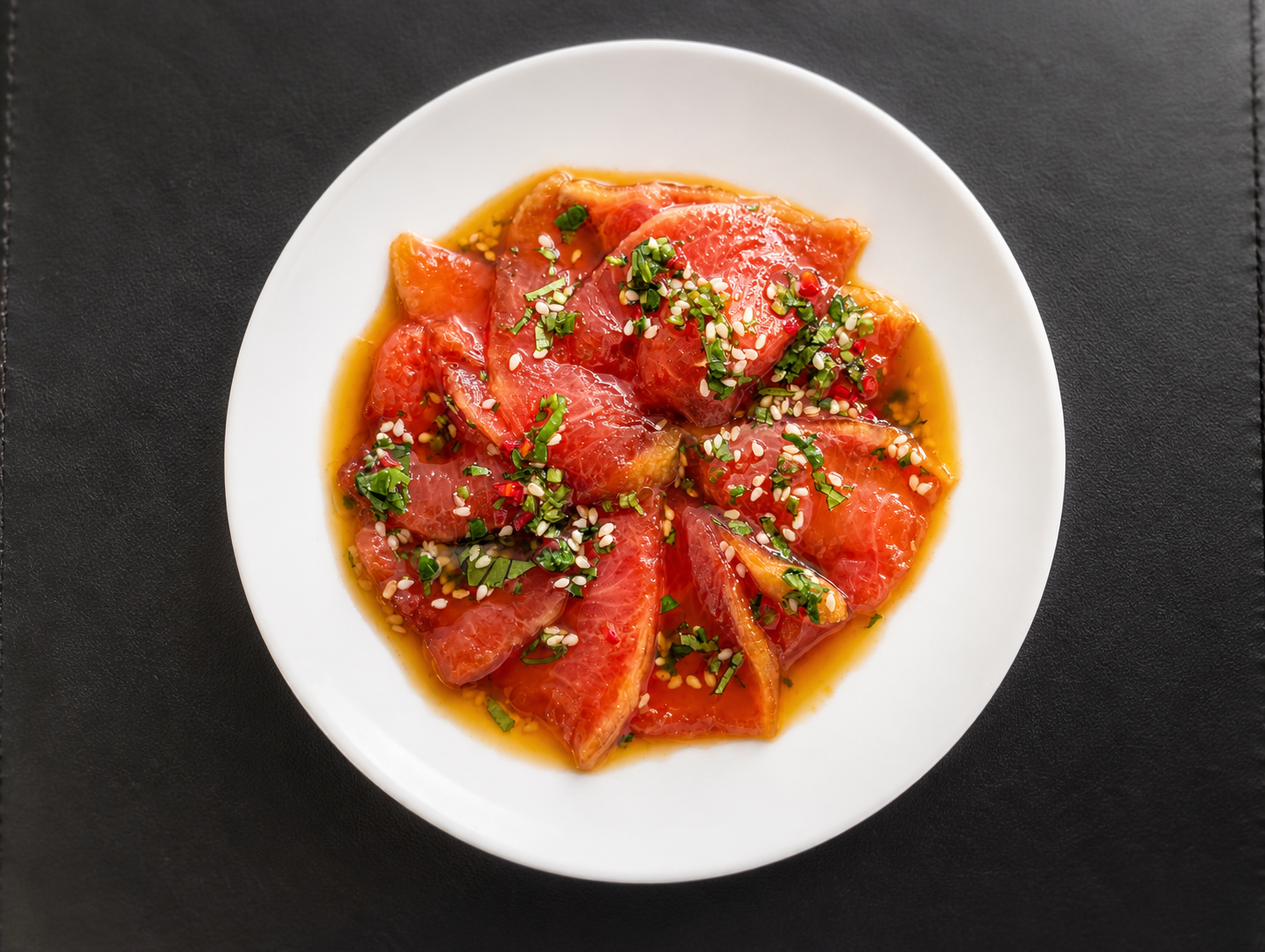 Plate of sliced tuna sashimi garnished with chopped green onions, sesame seeds, and red pepper flakes, served with a soy-based sauce.