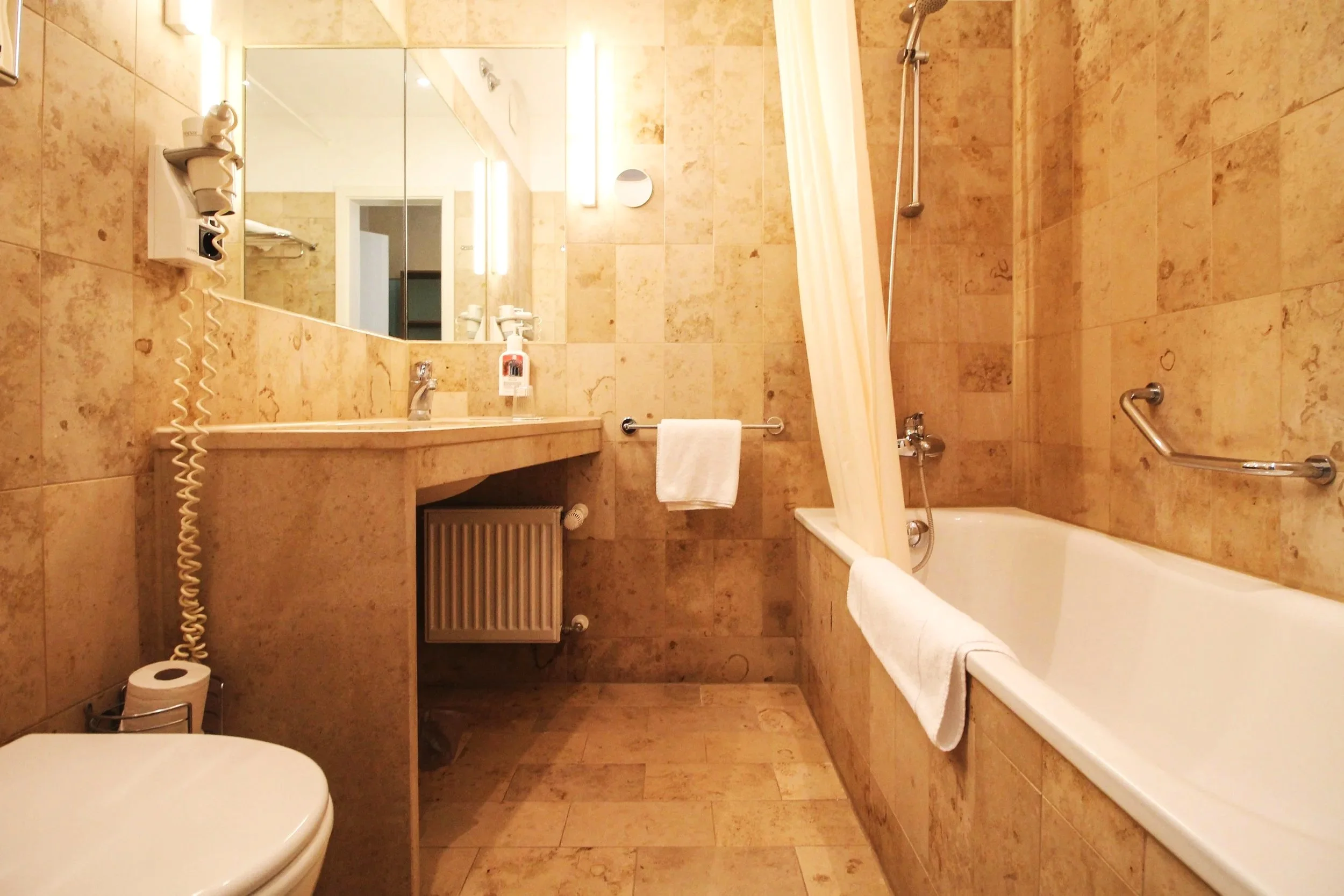 Badezimmer mit Dusche, Waschbecken, Spiegel, Handtuch und WC, alles in beige Tönen.