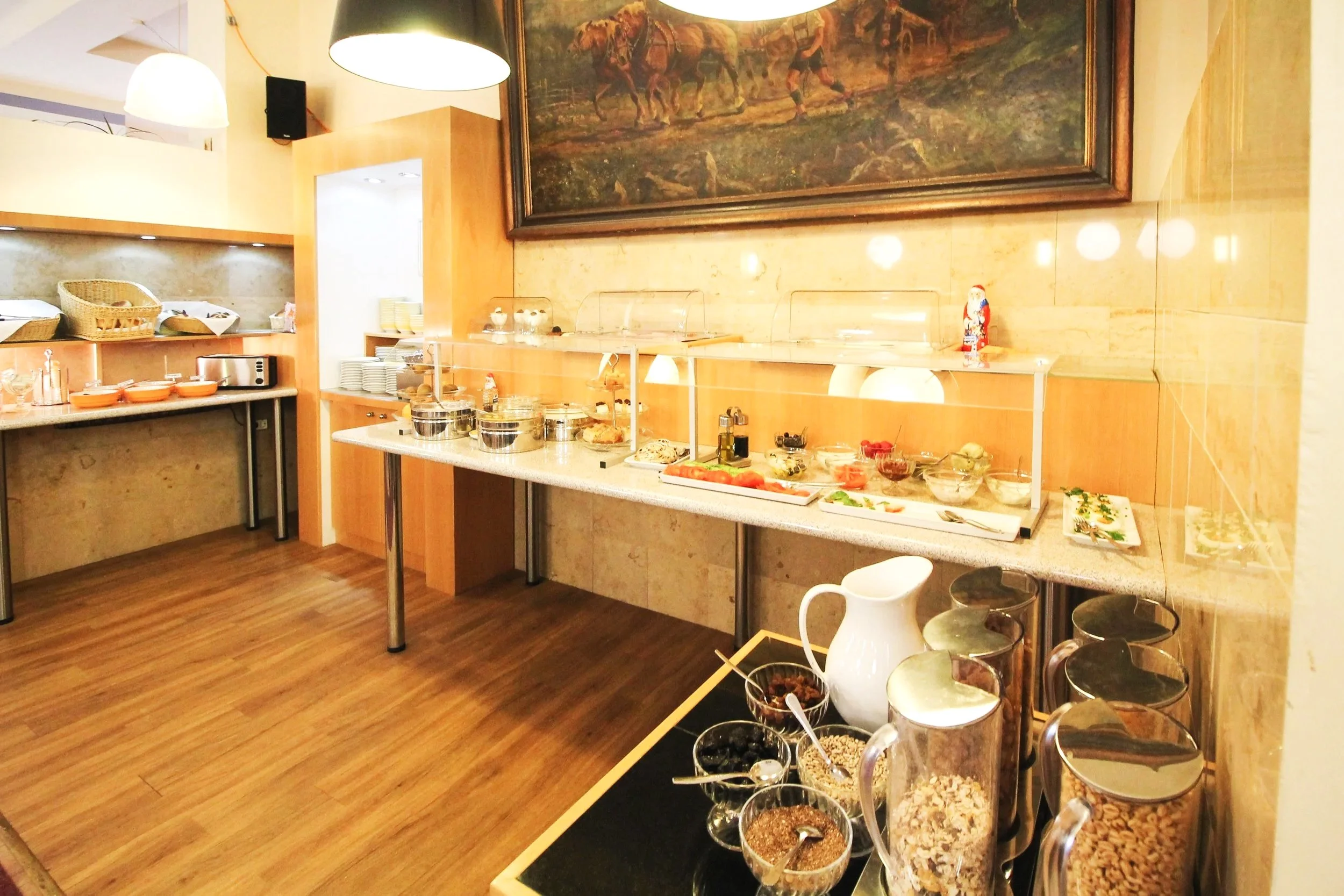 Buffet mit verschiedenen Lebensmitteln und Snacks, in einem Restaurant mit Holzfußboden und Wanddekoration, darunter ein großes Gemälde.