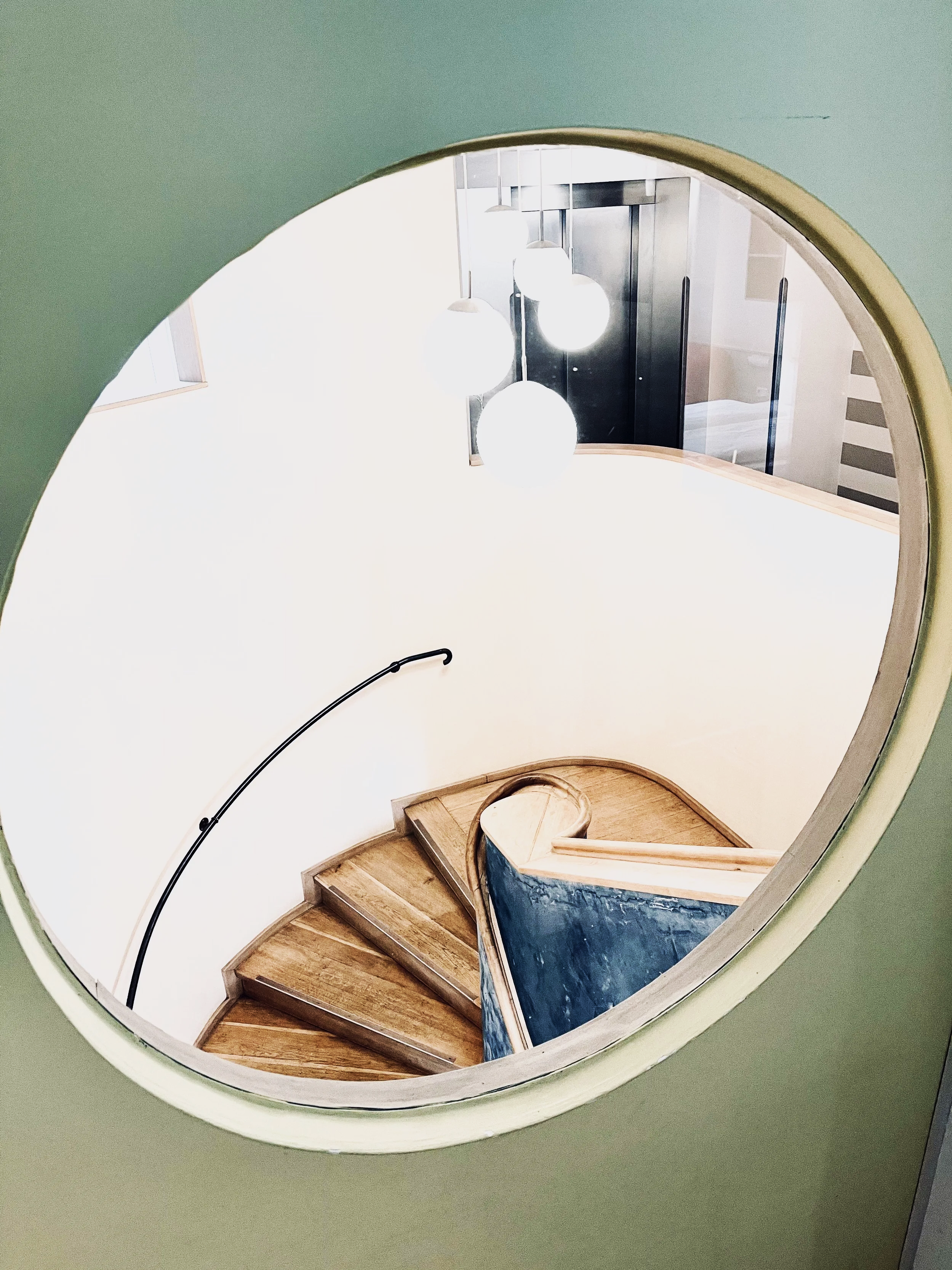 Ein Blick in einen spiralförmigen Holztreppenaufgang mit fünf Stufen, die zu einer oberen Etage führen. Die Treppe ist aus Holz gefertigt und es hängen mehrere weiße runde Lampen an der Decke, die den Raum beleuchten.