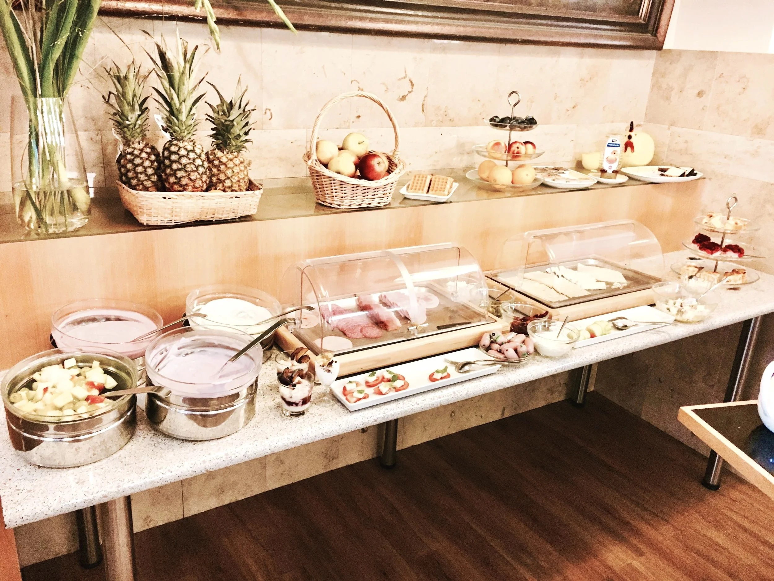 Frühstücksbuffet mit Obst, Waffeln, Joghurt, Aufschnitt und Desserts an einem Frühstückstisch.