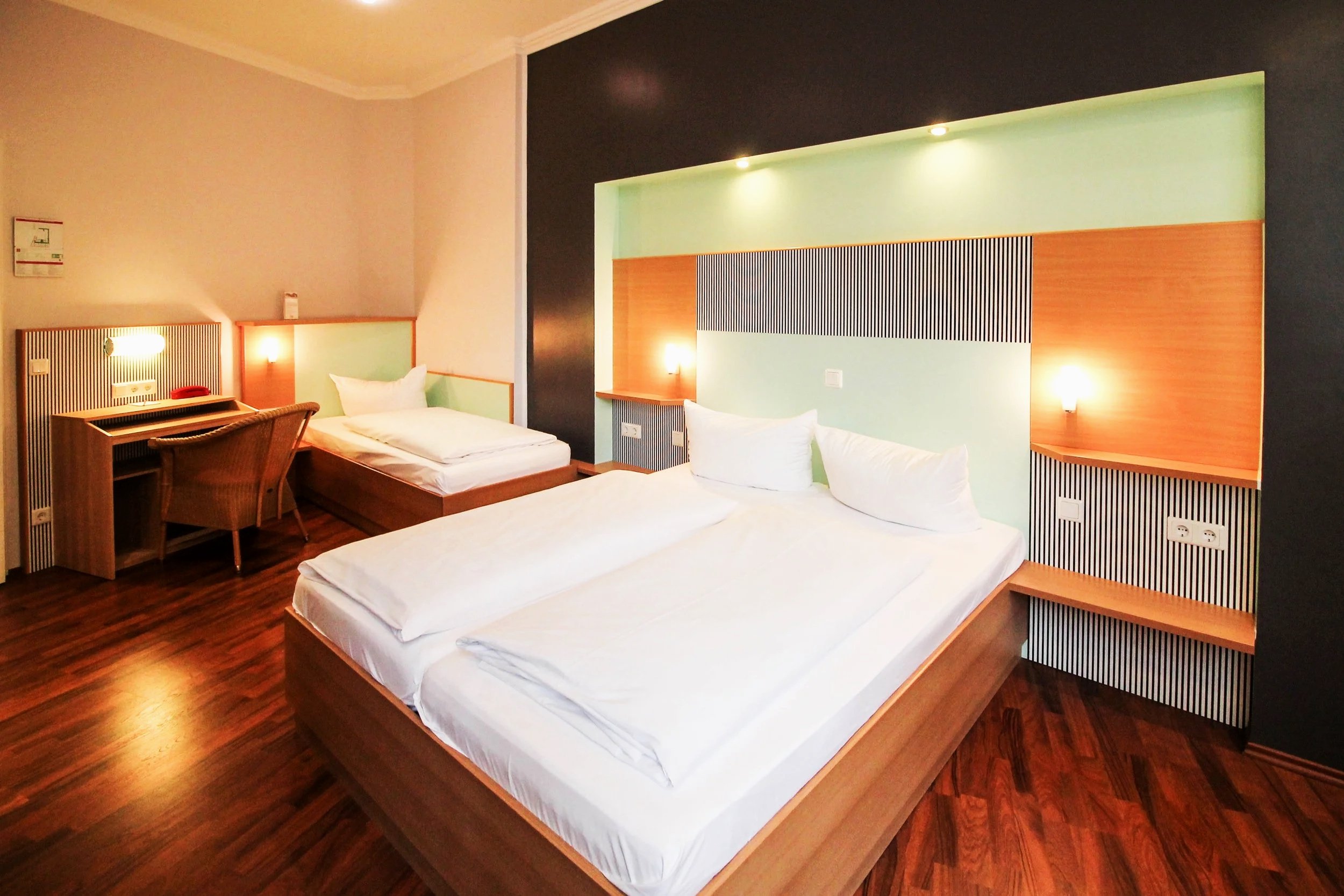 Ein Hotelzimmer mit zwei zusammengeschobenen Betten, Holzenelementen und einer hellen Wand im Hintergrund.