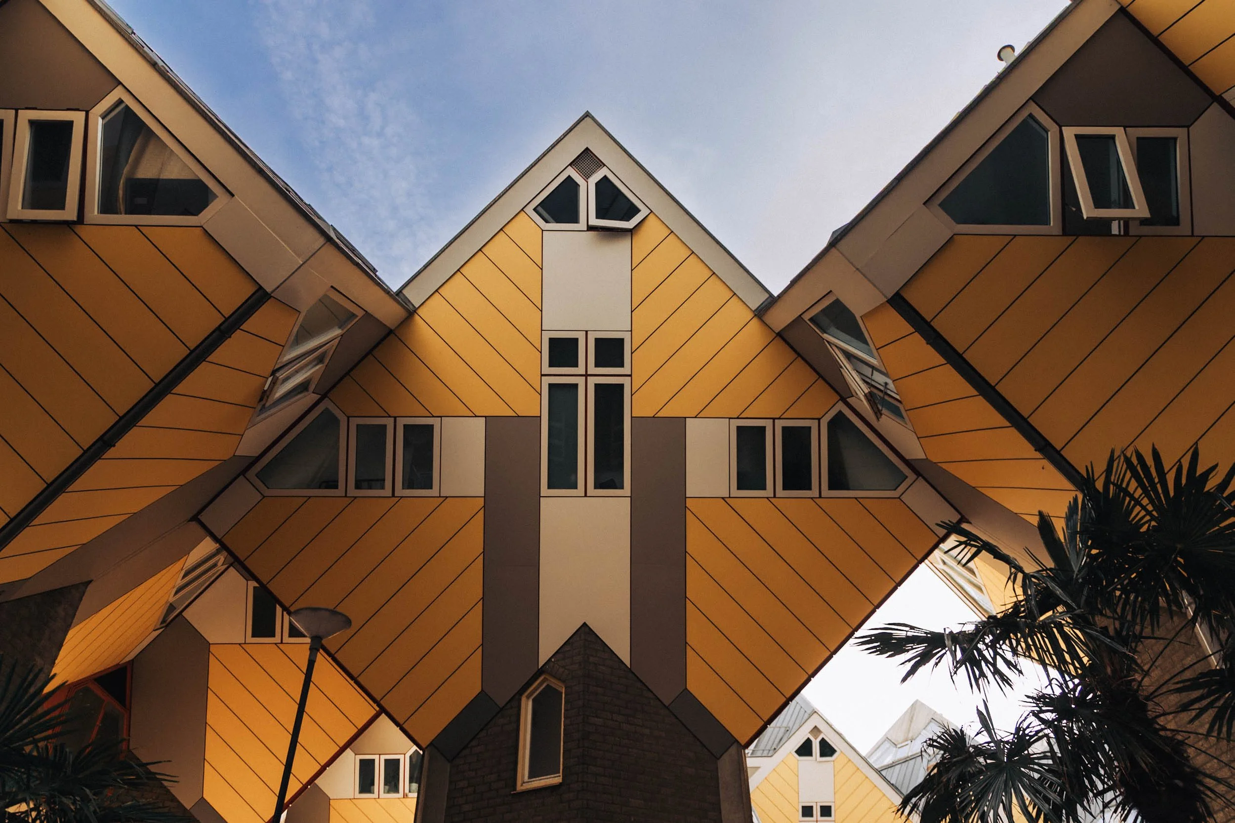 Looking up at the Cubist-style yellow and gray apartment buildings with angular shapes and multiple windows, with a partly cloudy sky in the background.