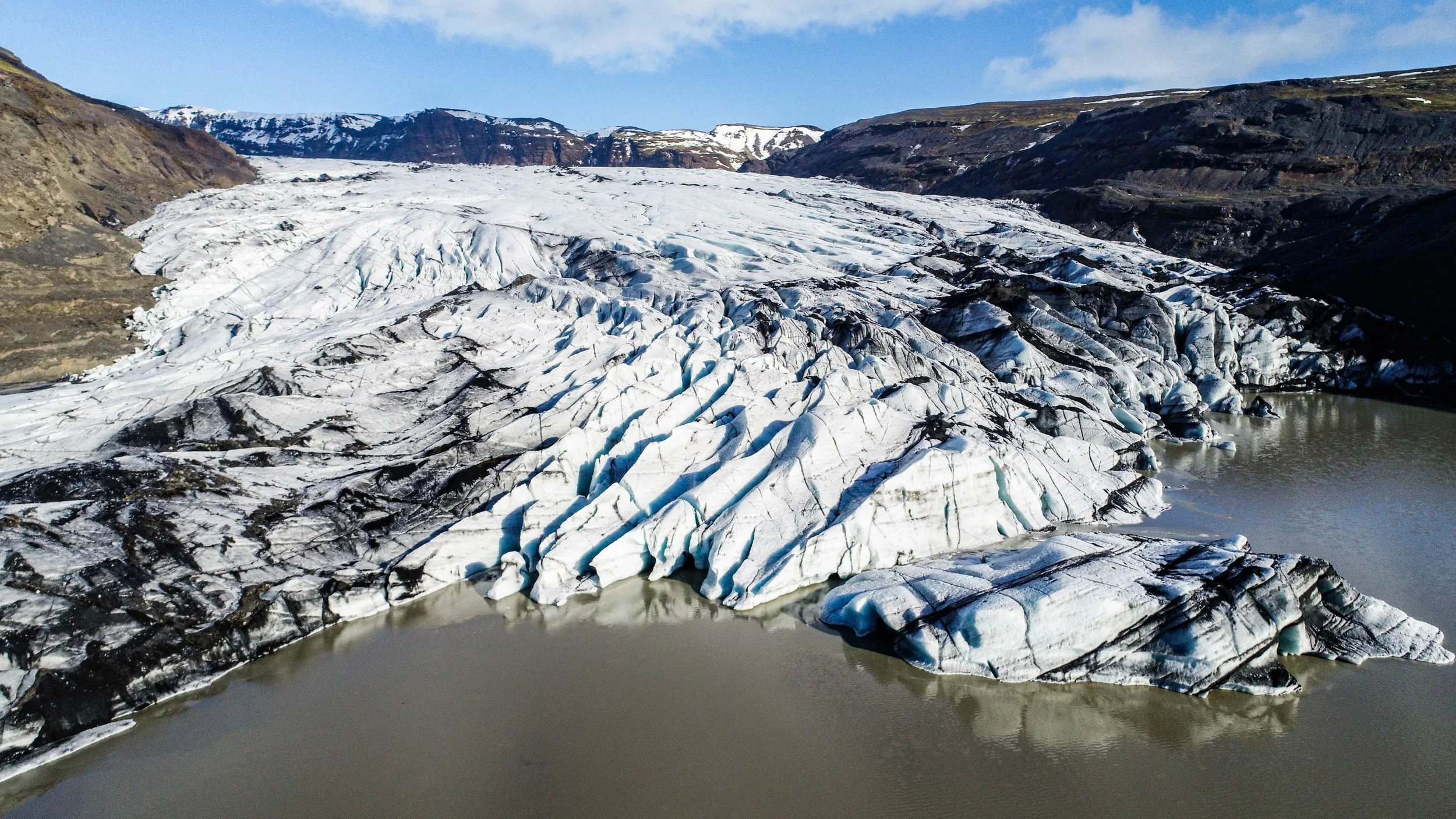 A glacier melting into a lake in a mountainous area with snow on the peaks in the background.