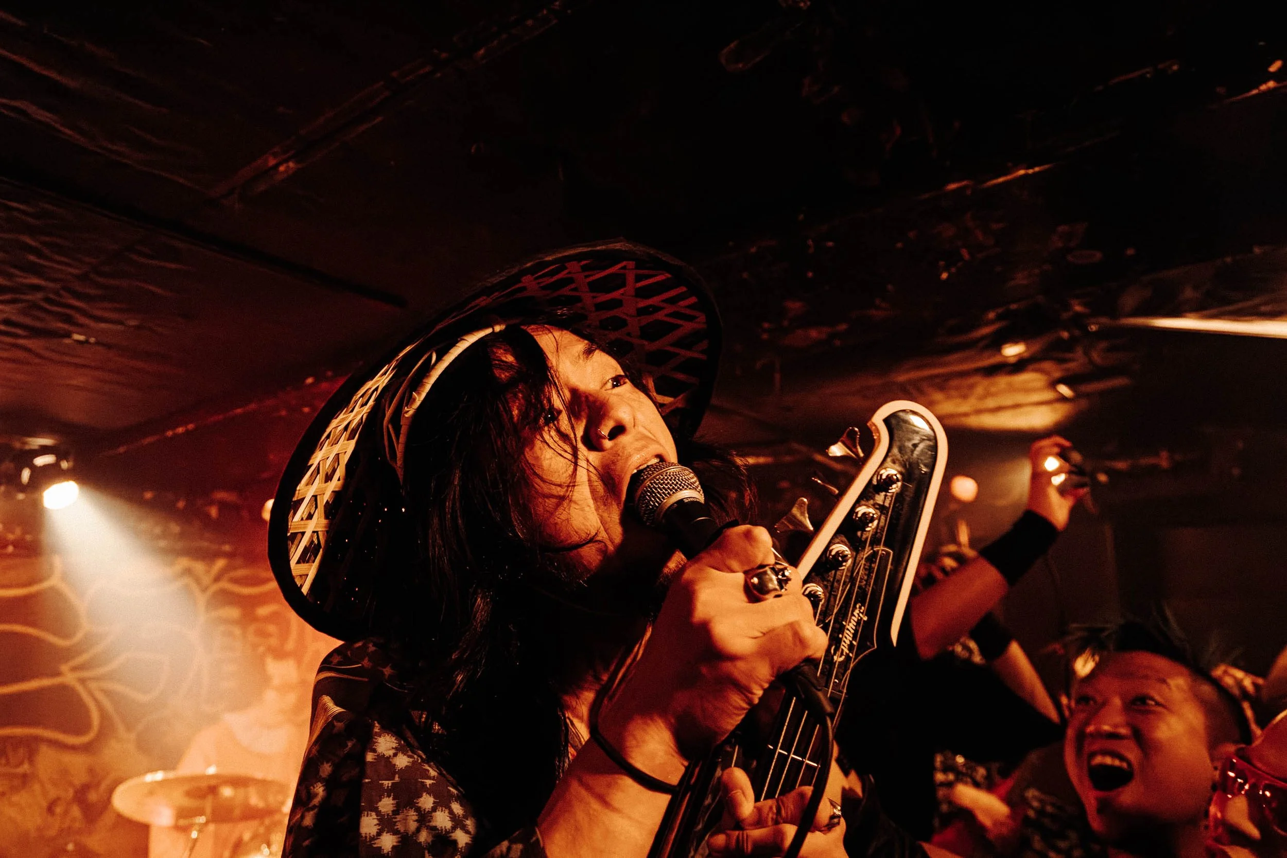 A woman singing into a microphone, wearing a cowboy hat, surrounded by an energetic crowd in a dimly lit venue.
