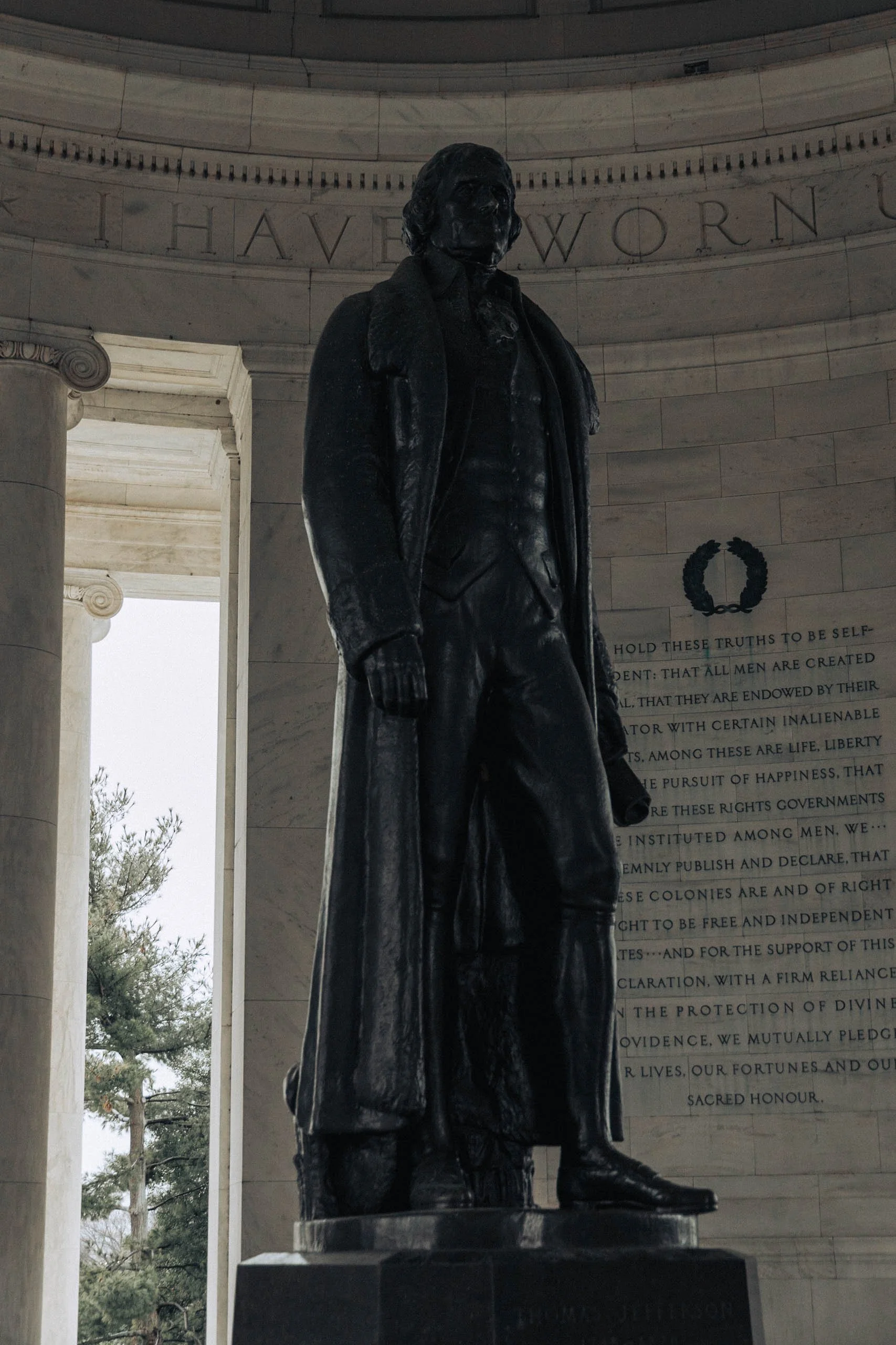 Statue of Abraham Lincoln in the Lincoln Memorial, standing with a long coat and fingerless gloves, against a marble wall with inscriptions.