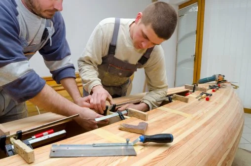 Two men working on a wood project, using clamps and tools to assemble a large wooden piece.