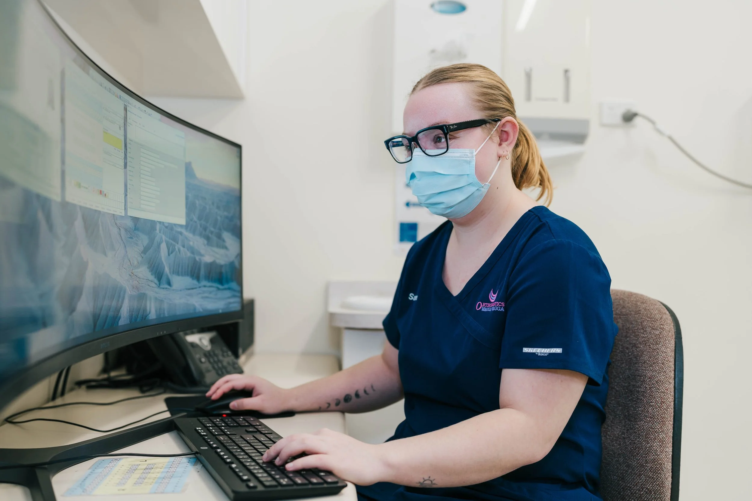 Dental Assistant working at a computer in a clinical setting.