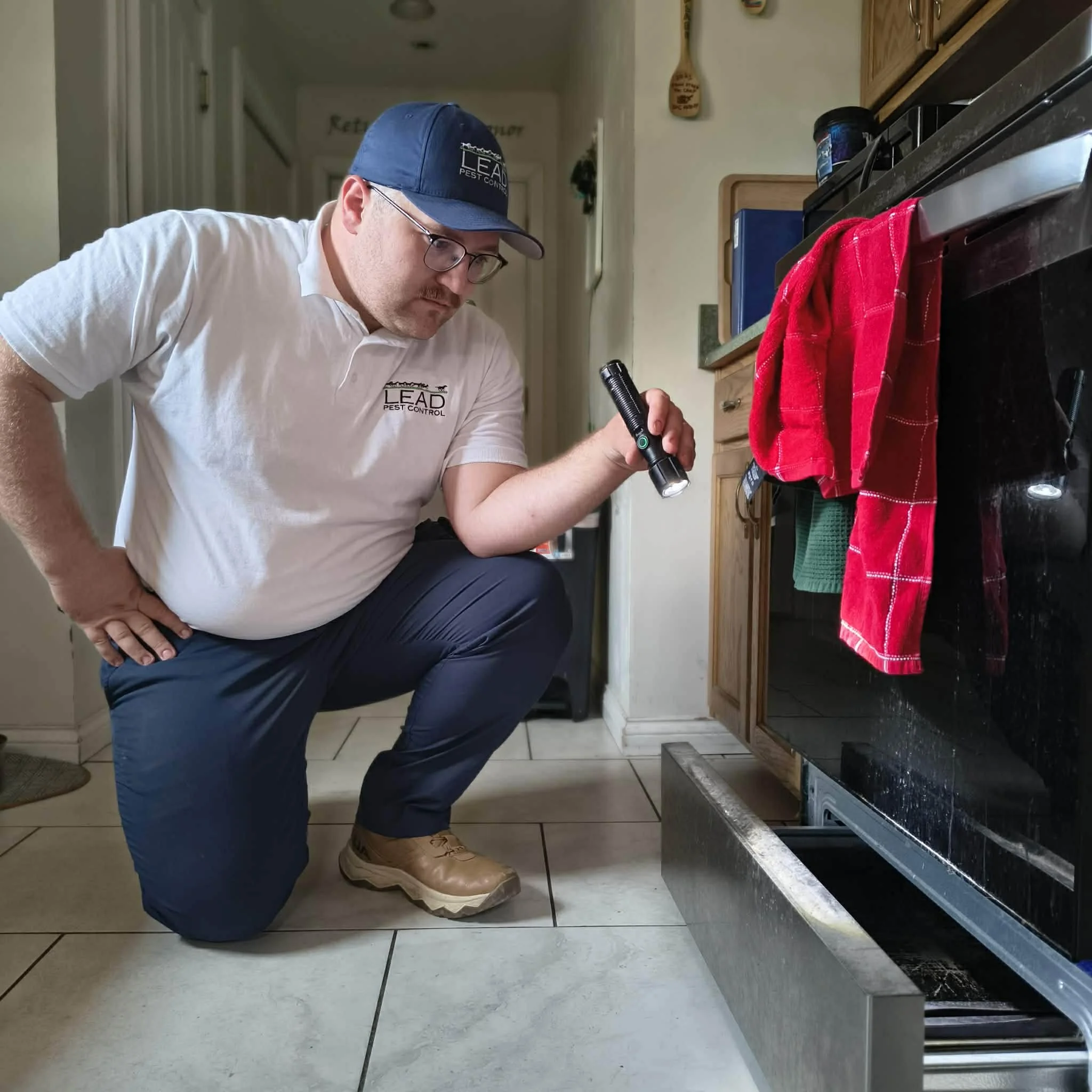 Pest control technician inspecting under stove for pest activity in kitchen in Elizabethtown KY